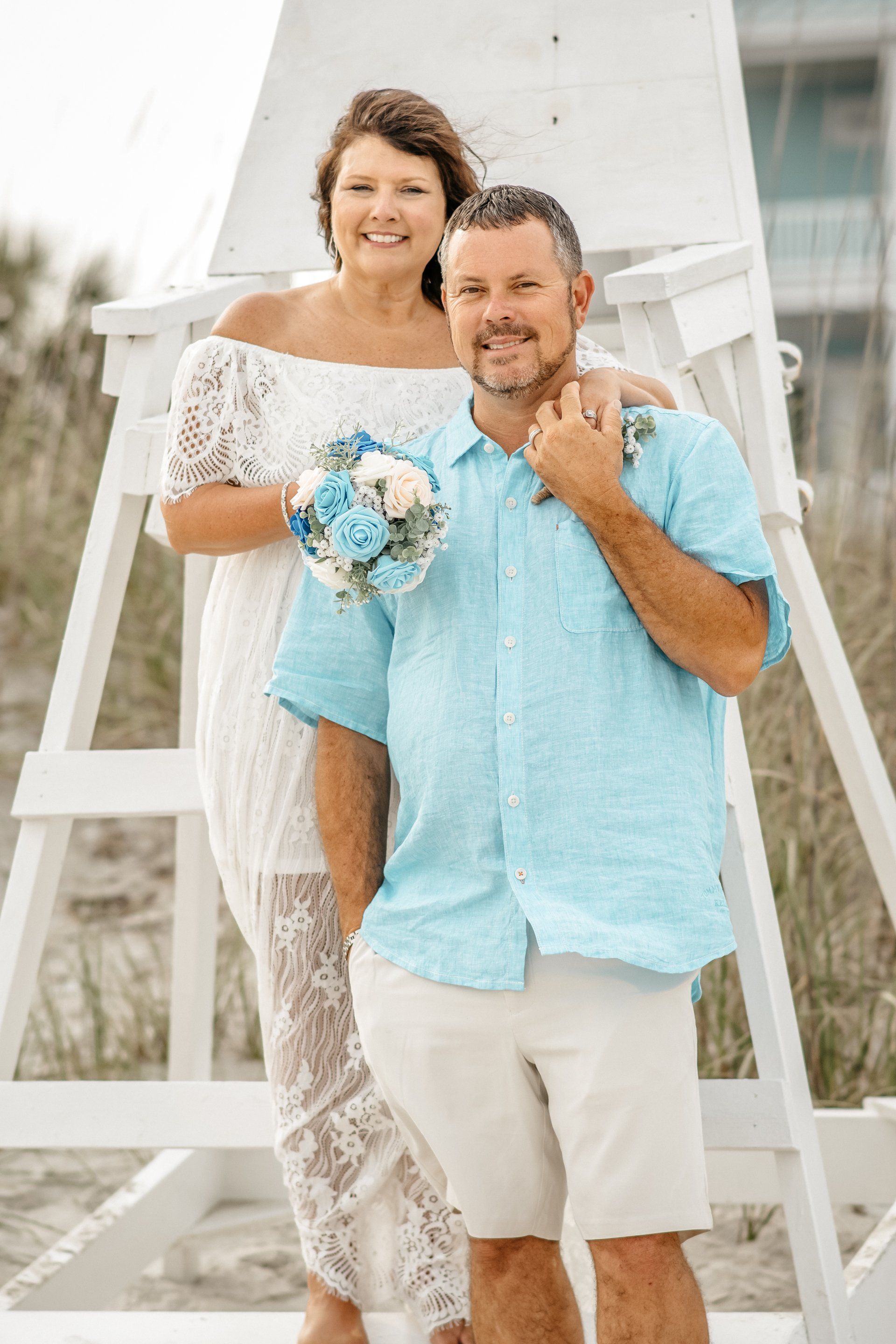 A bride and groom are posing for a picture in front of a lifeguard tower on the beach.