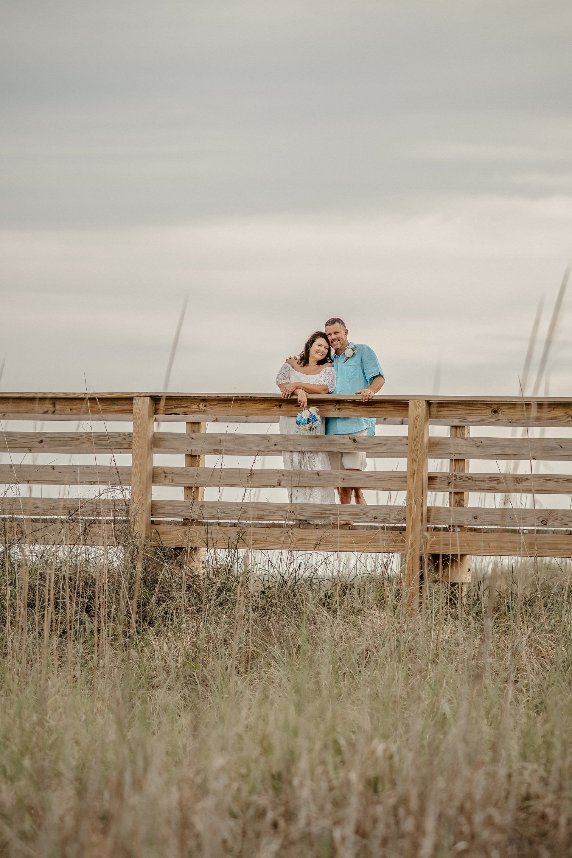 A man and woman are standing on a wooden bridge over a field.