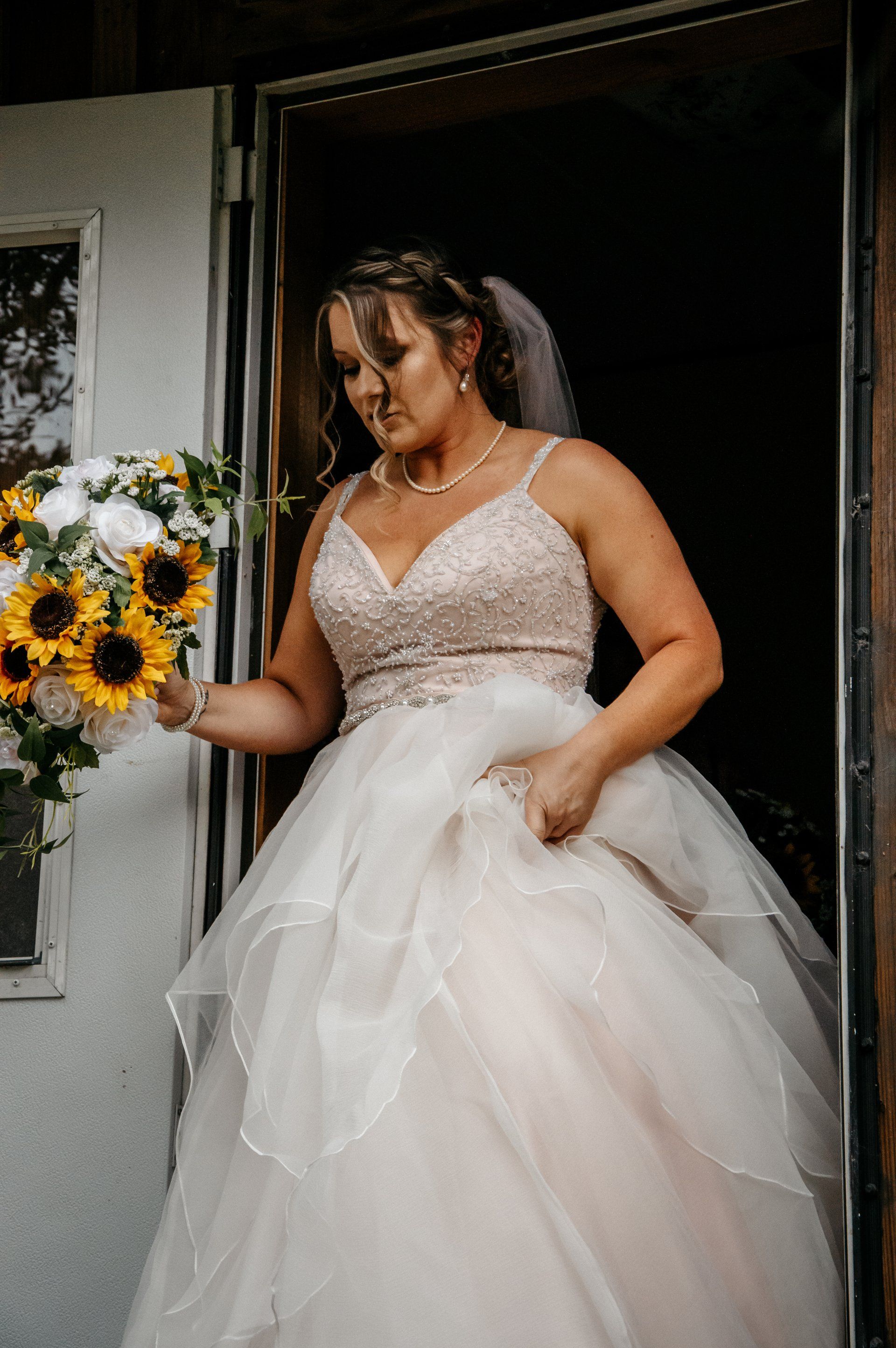 A bride in a wedding dress is holding a bouquet of sunflowers.