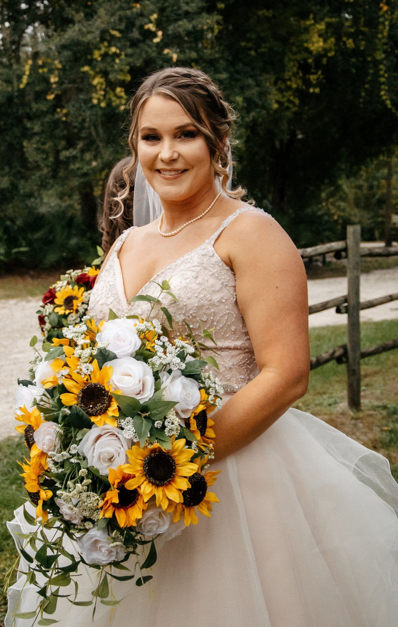 A bride in a wedding dress is holding a bouquet of sunflowers and roses.