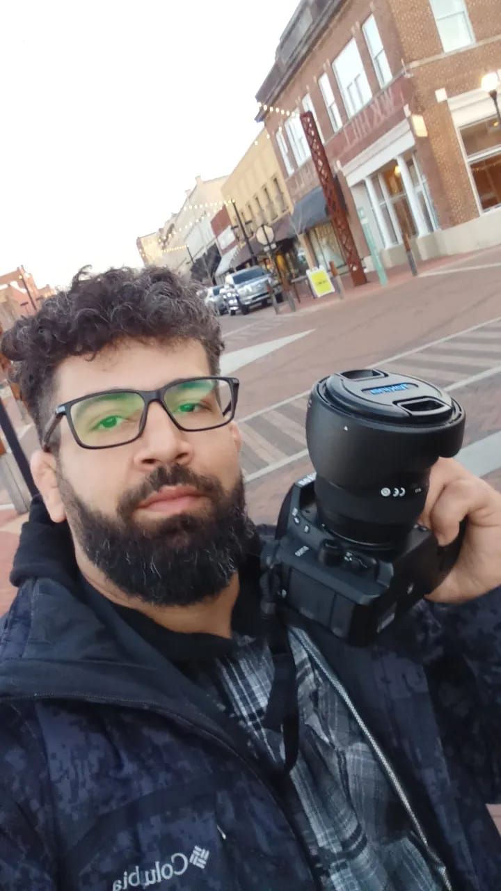 A woman, Morgan René Doscher (owner of Mo Knows Marketing, LLC DBA Mo Knows Art) in an orange dress is holding a nikon camera