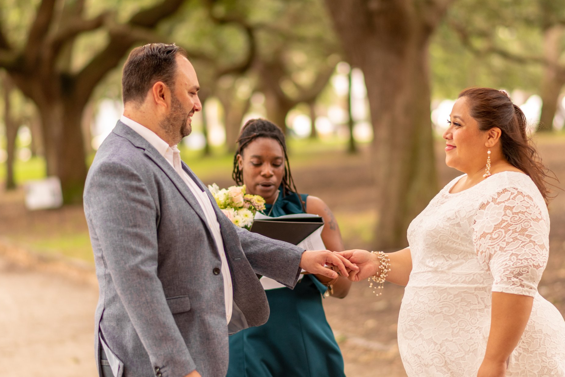 A bride and groom are holding hands during their wedding ceremony in a park.