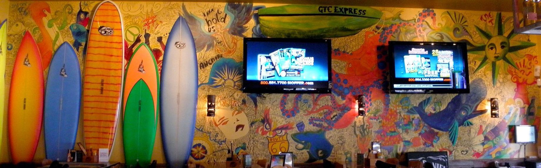 A wall with surfboards painted on it and two televisions