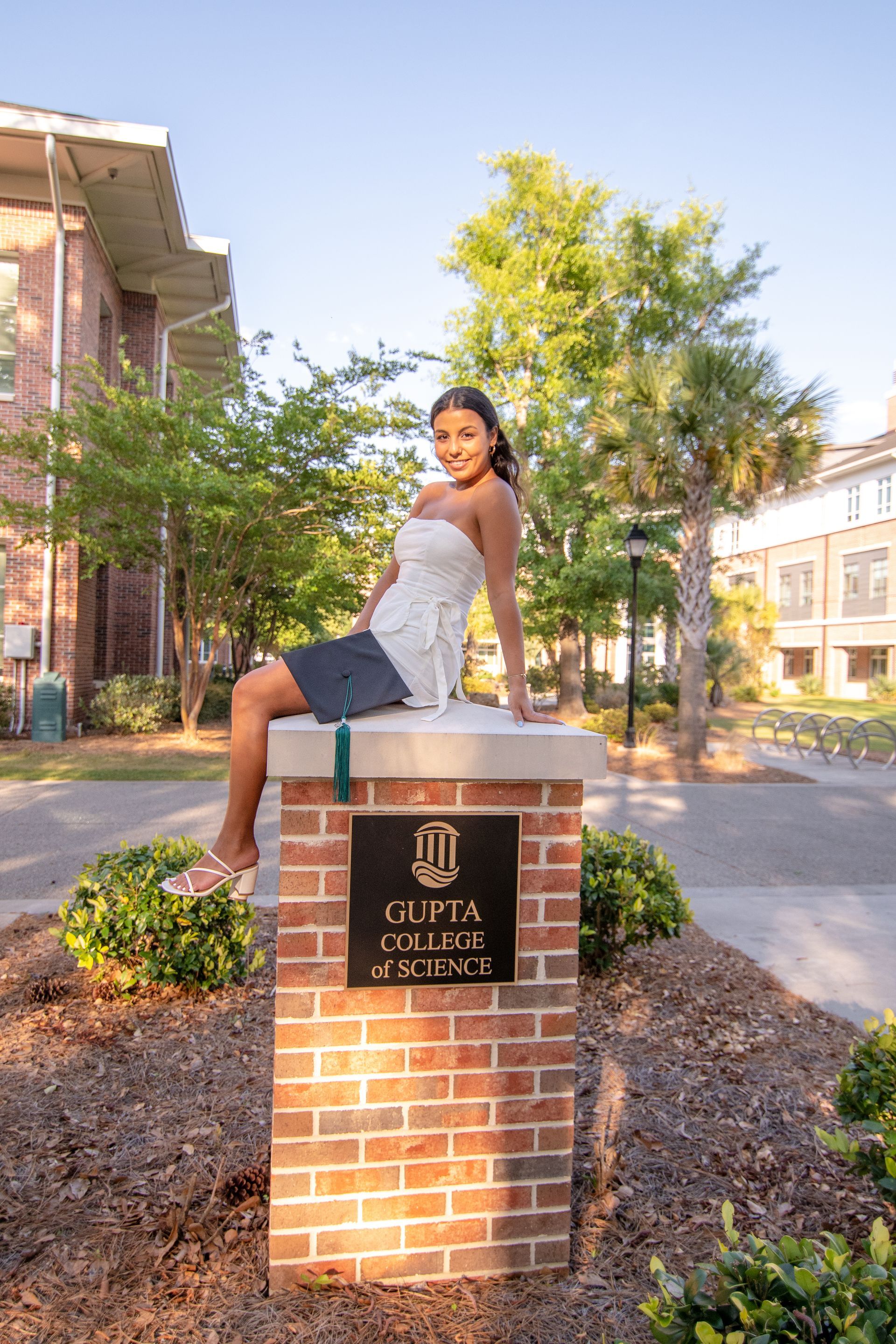 A woman is sitting on a brick pillar in front of a building.