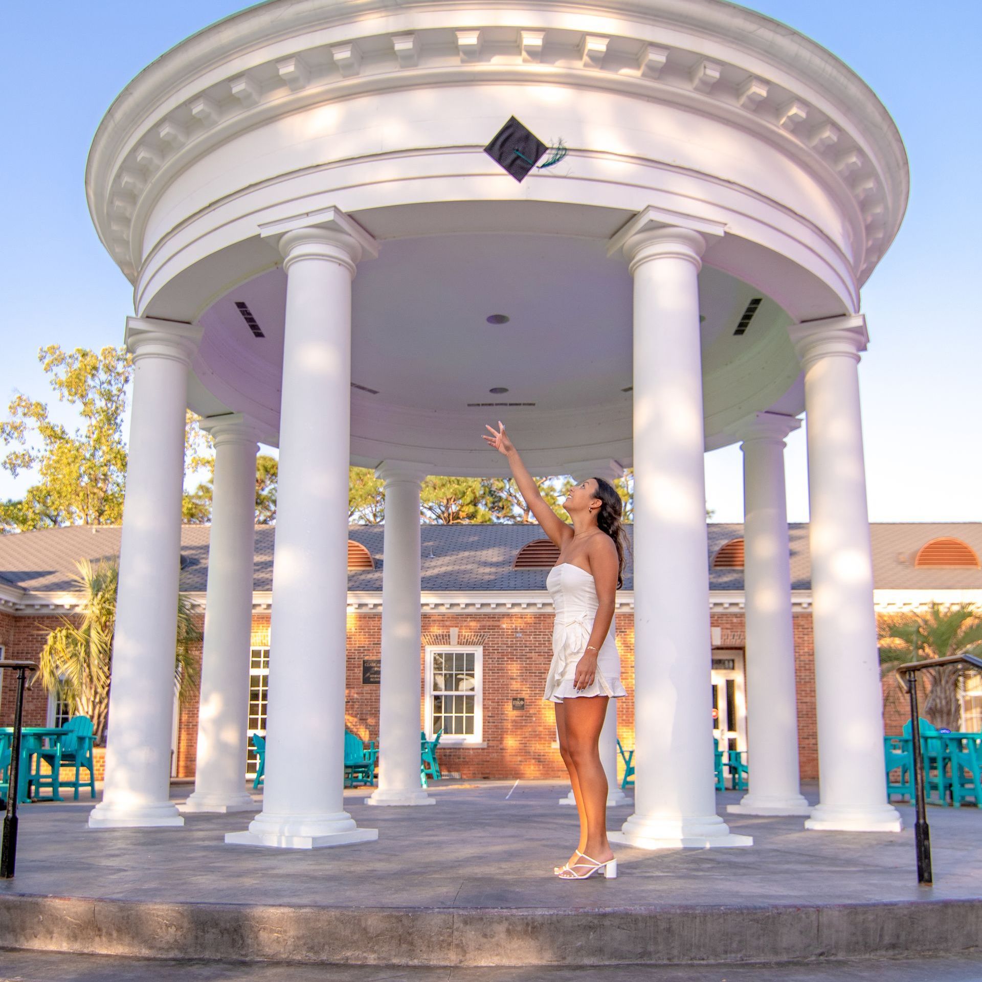 A woman in a white dress is throwing a graduation cap in the air