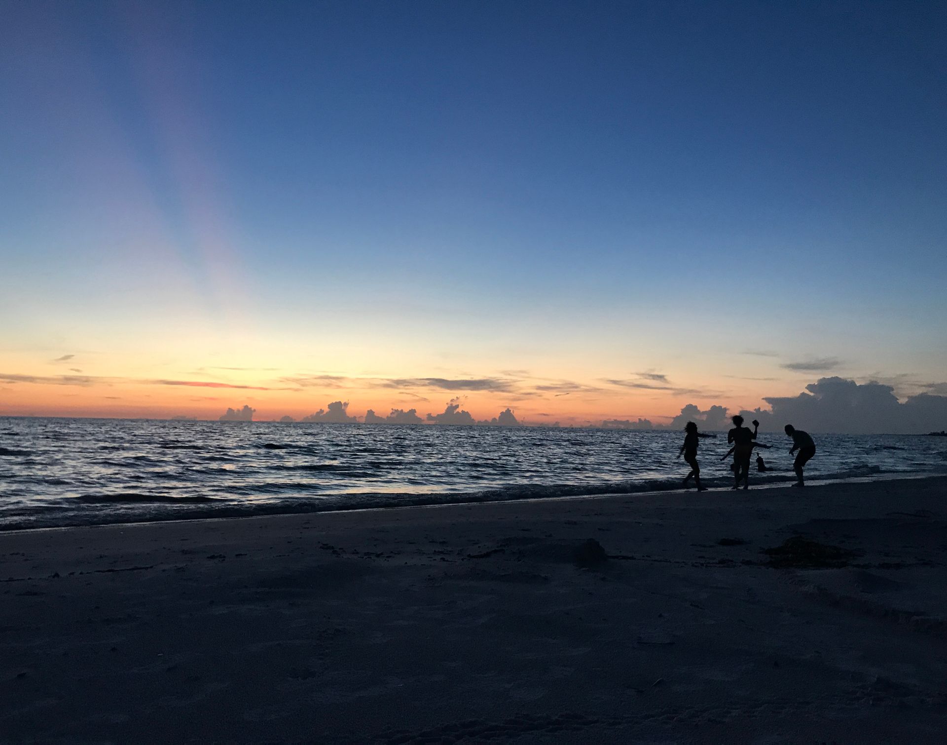 A group of people are standing on a beach at sunset.