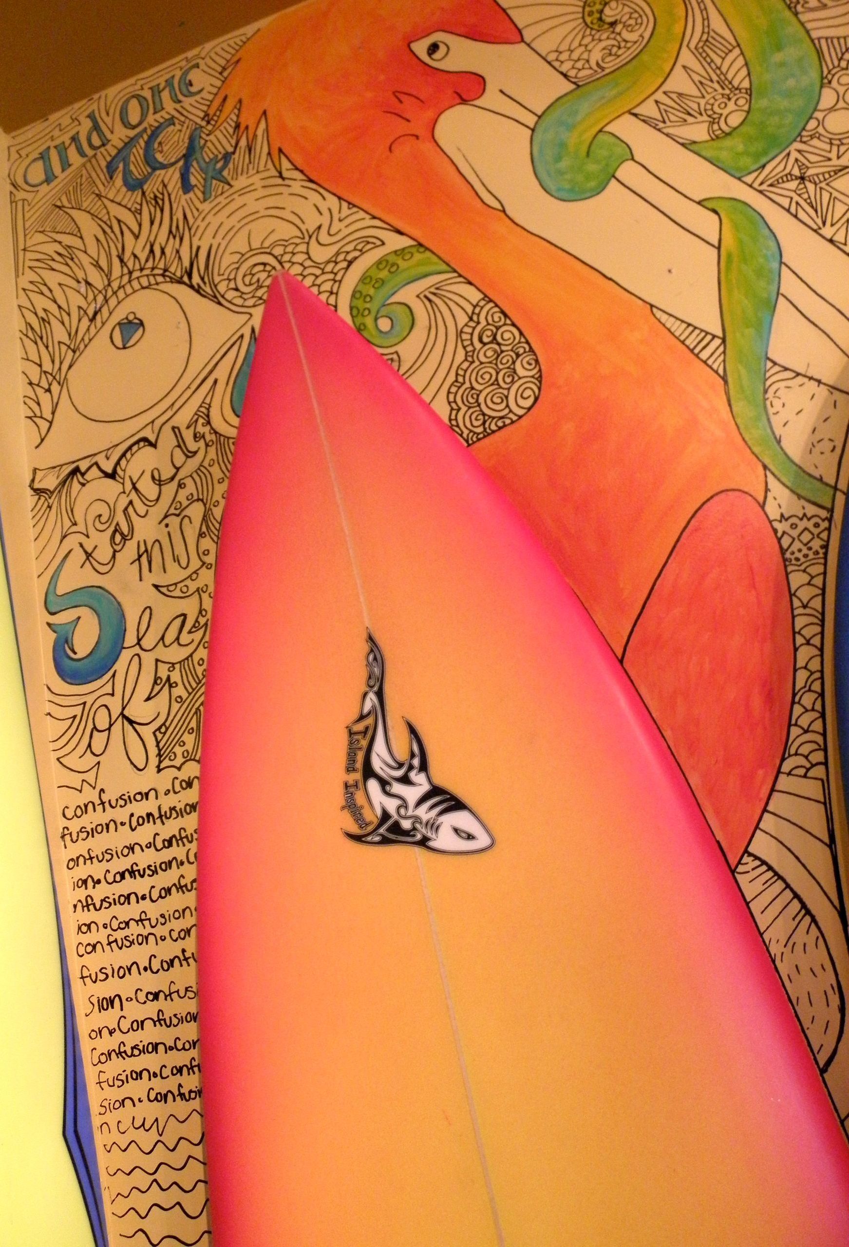 A pink surfboard sits in front of a drawing of a flamingo