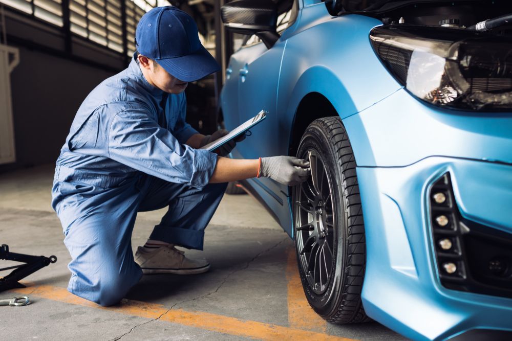 A mechanic is working on a blue car in a garage.