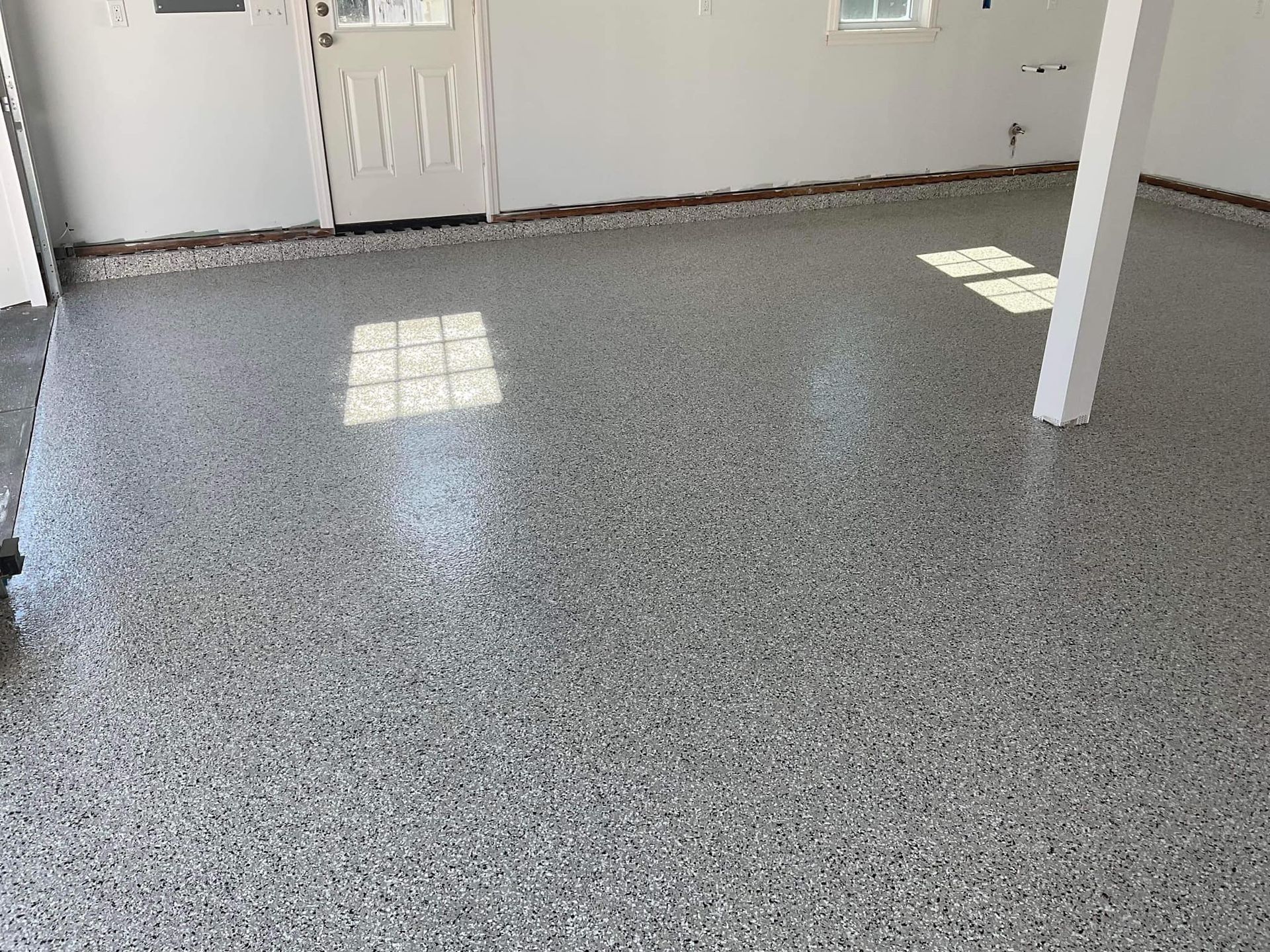 Garage interior with a speckled gray epoxy floor, white walls, and a door.