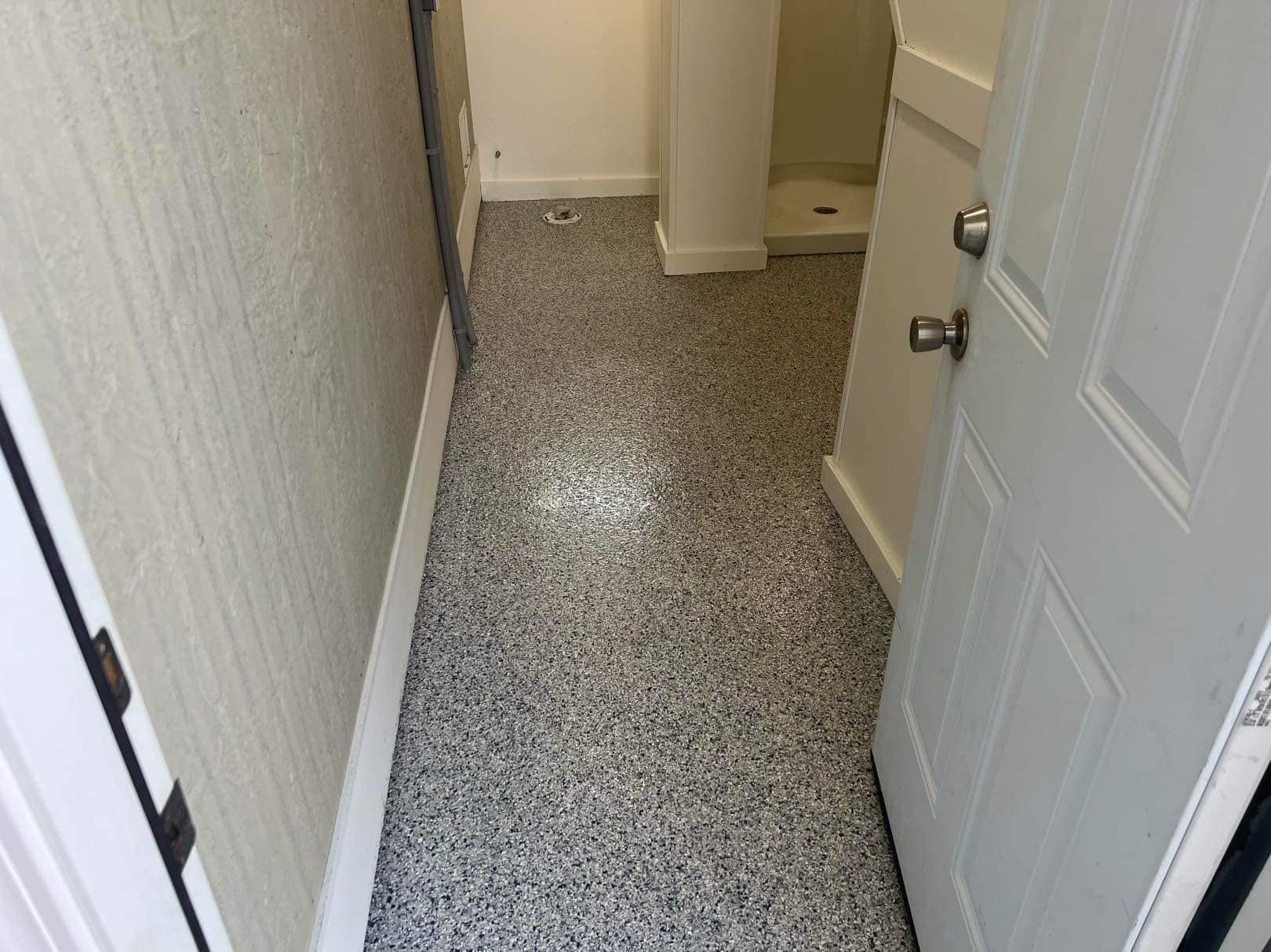 Narrow hallway with speckled gray flooring, white walls, and an open white door.