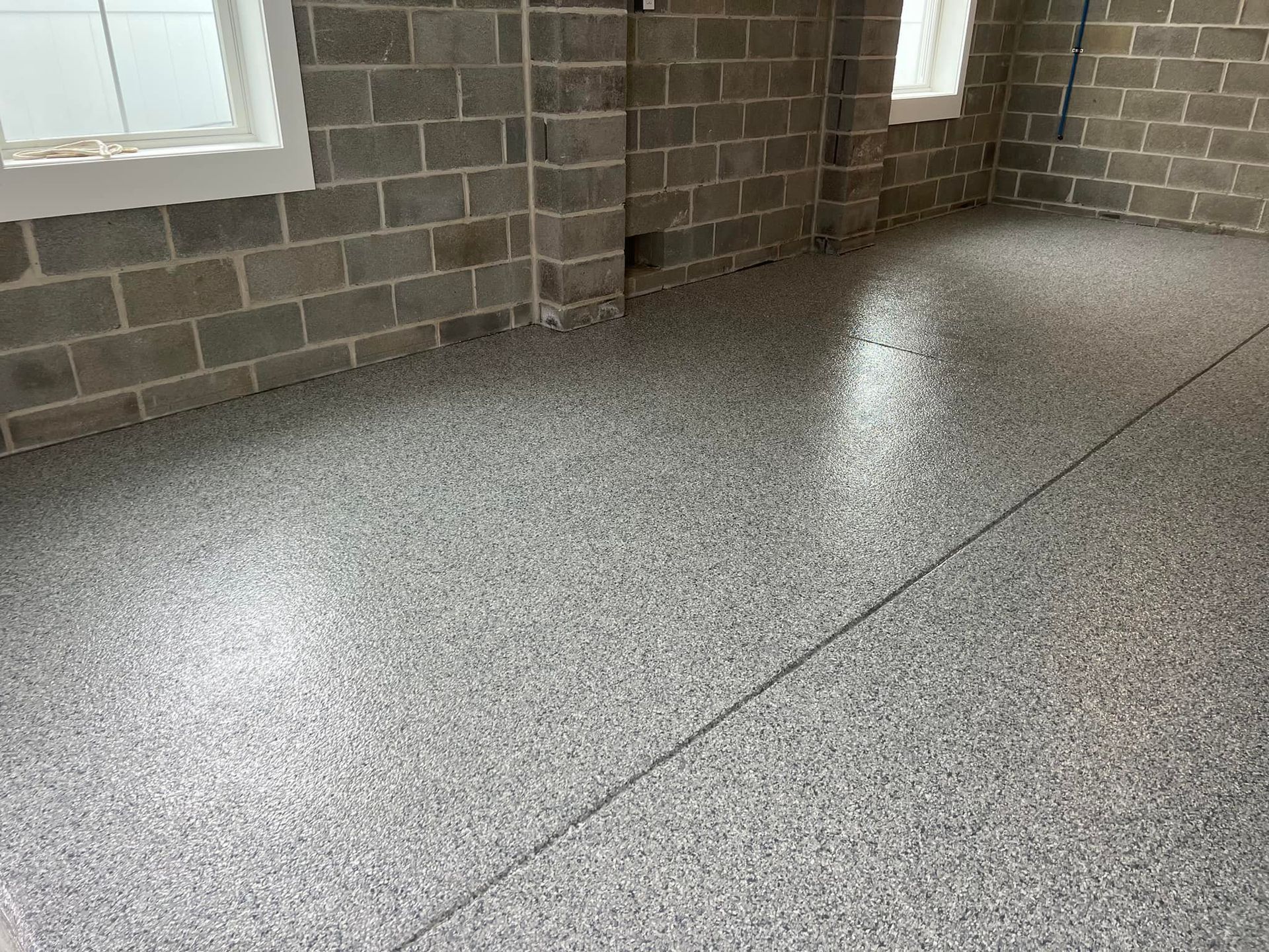 Gray epoxy floor in a room with gray cinder block walls and white-framed windows.