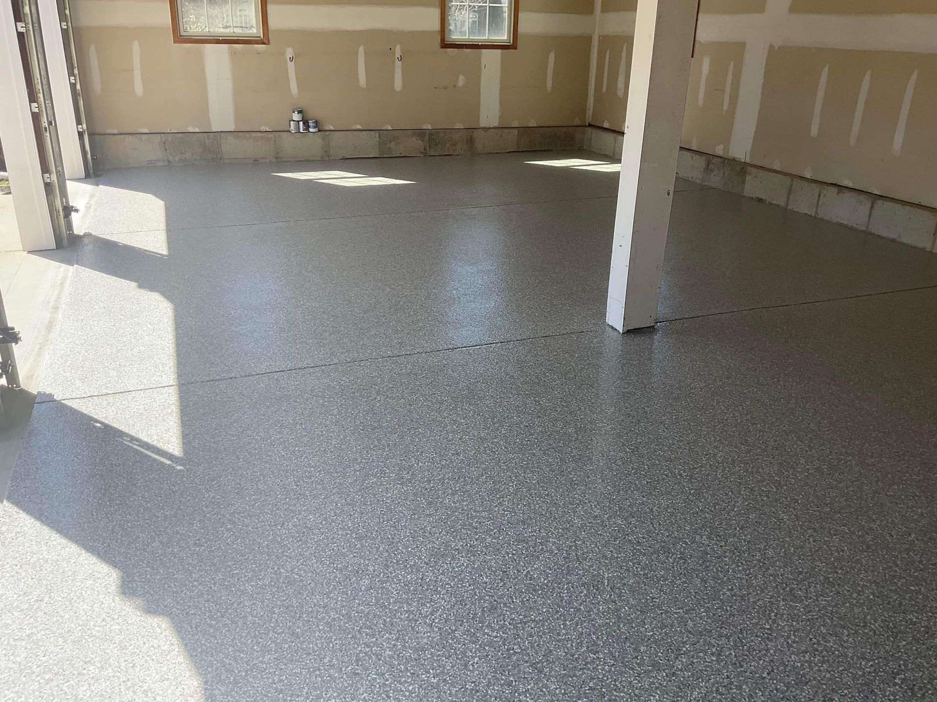 Garage with a gray epoxy floor, beige walls, and two pillars.