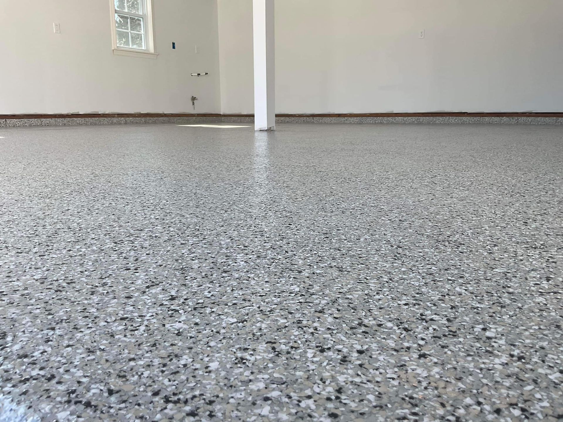 Gray and white speckled epoxy garage floor. White walls and a support beam.