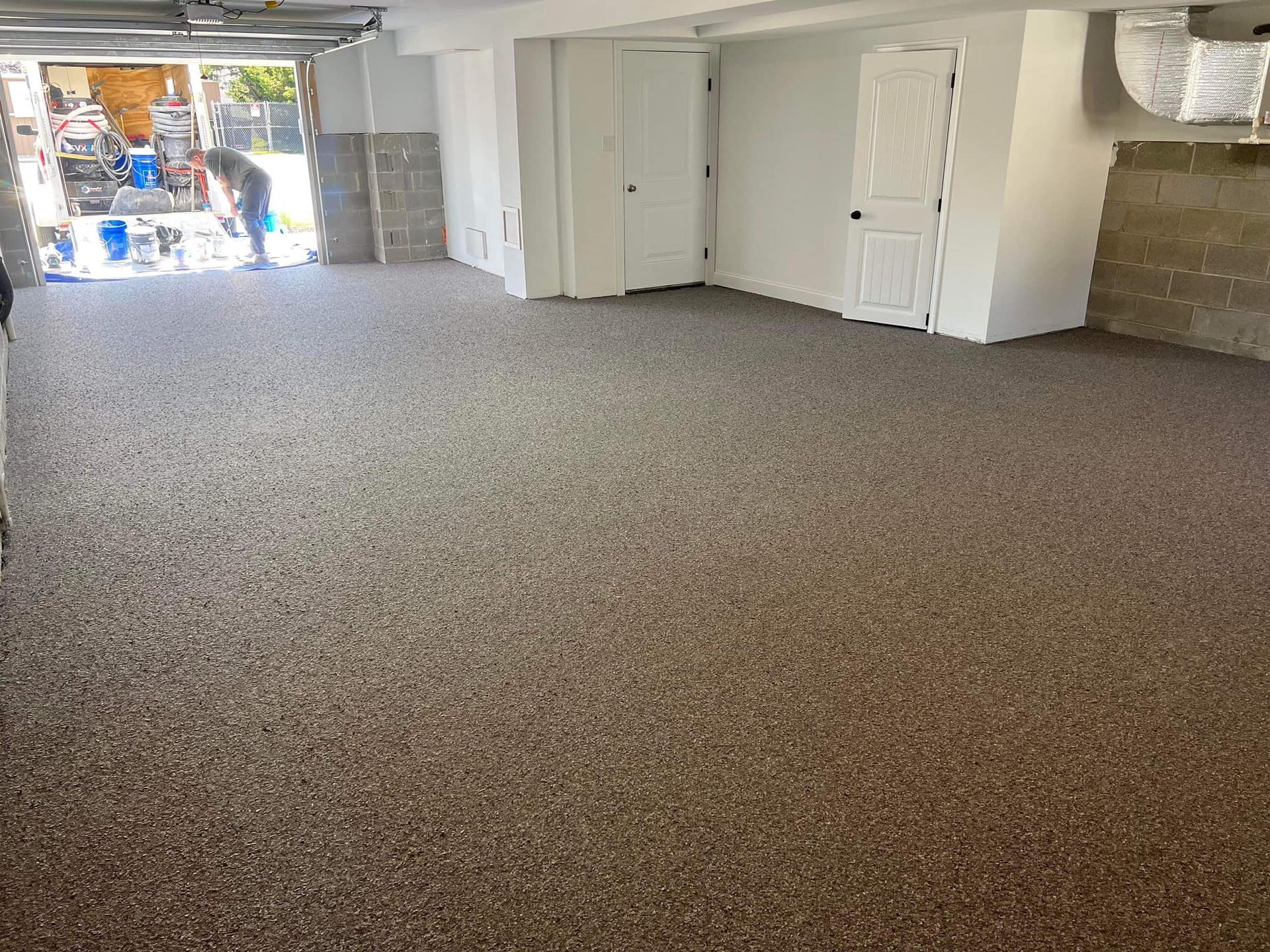 Garage floor with brown speckled coating. Two white doors. Sunlight streams in from open garage door.