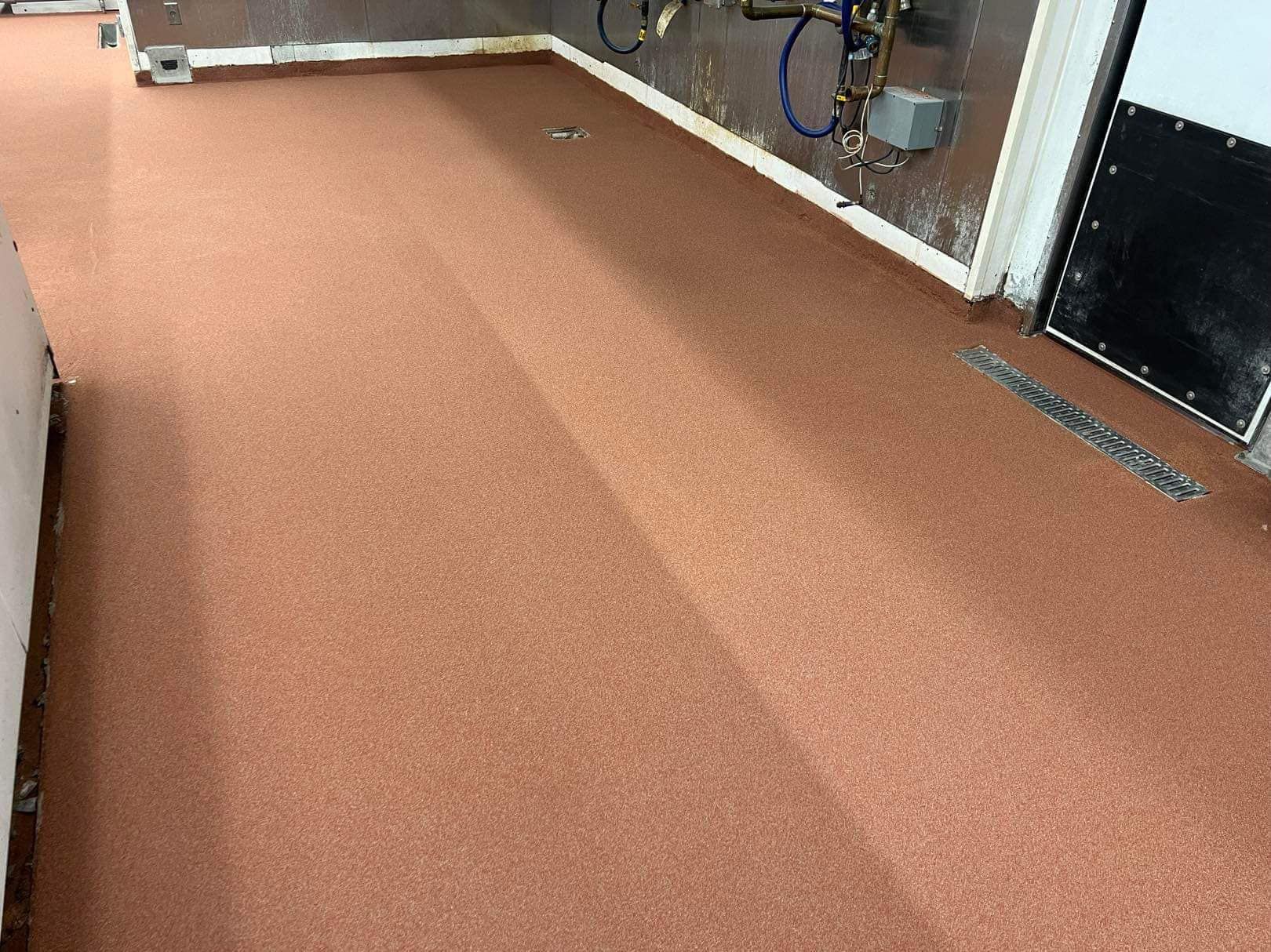 Red-toned, textured floor in a commercial space, with white trim along the walls.