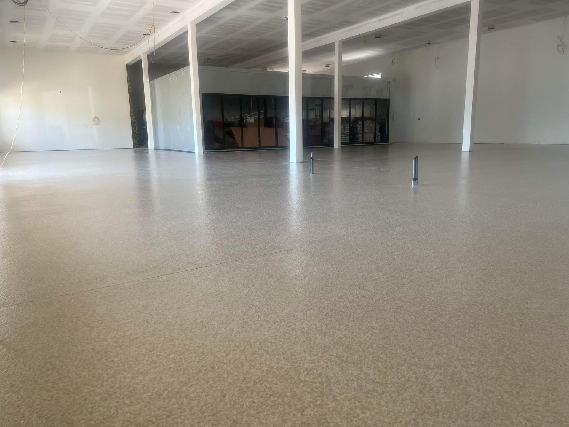 Large empty room with polished speckled floor, white columns, and neutral walls.