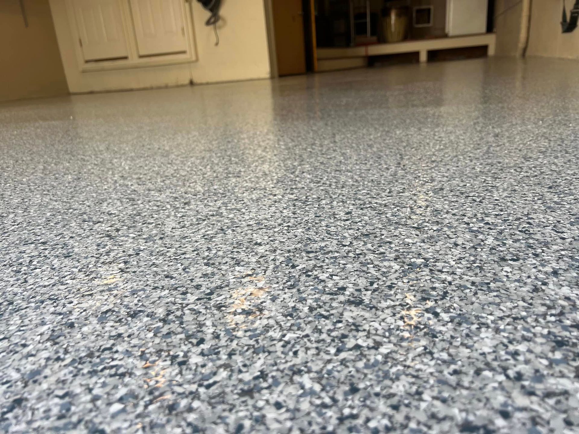 Granite-like epoxy floor in a garage, with a speckled blue, gray, and white pattern, reflecting light.