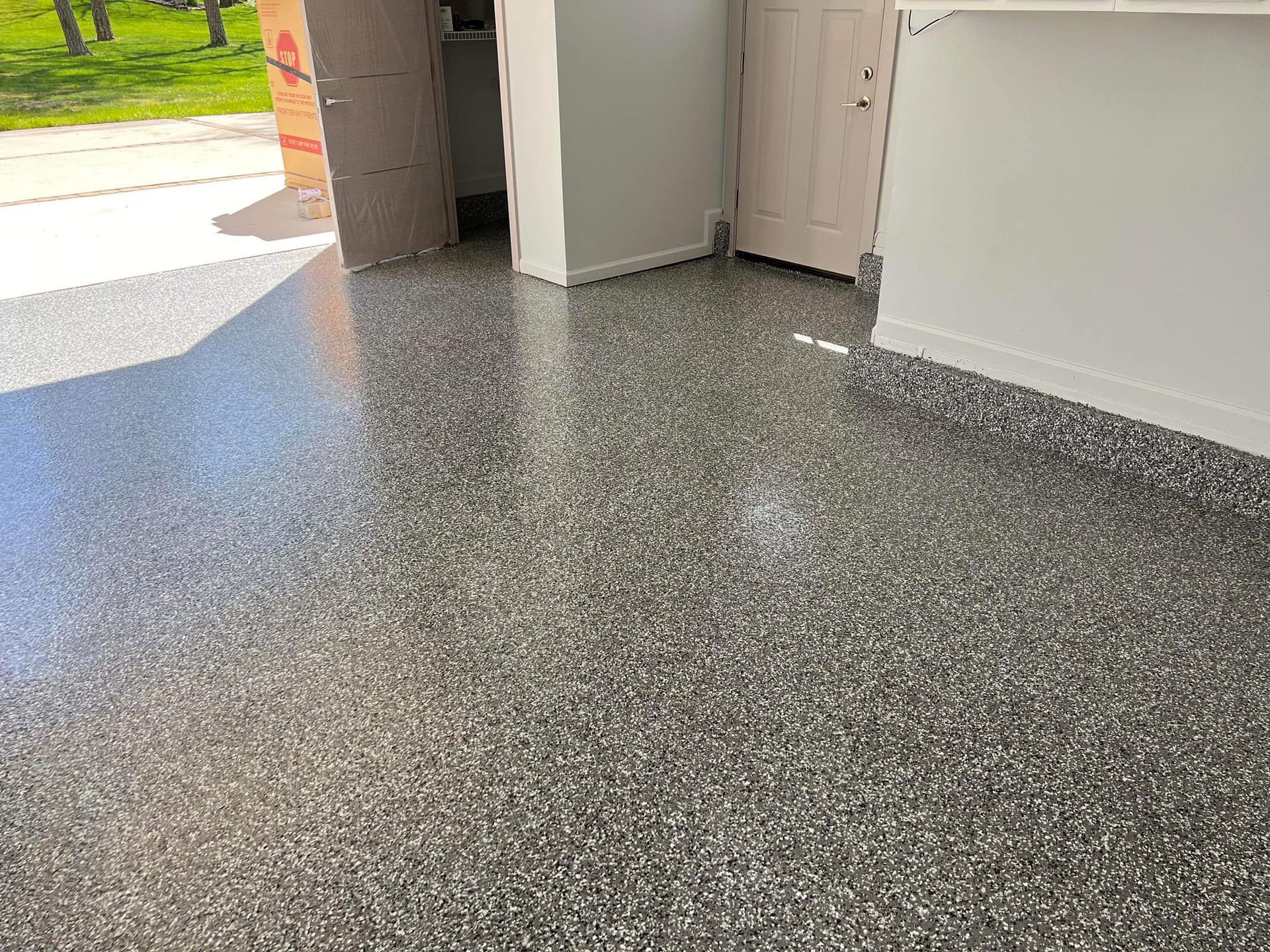 Garage floor with shiny speckled gray epoxy coating; white walls and a door.