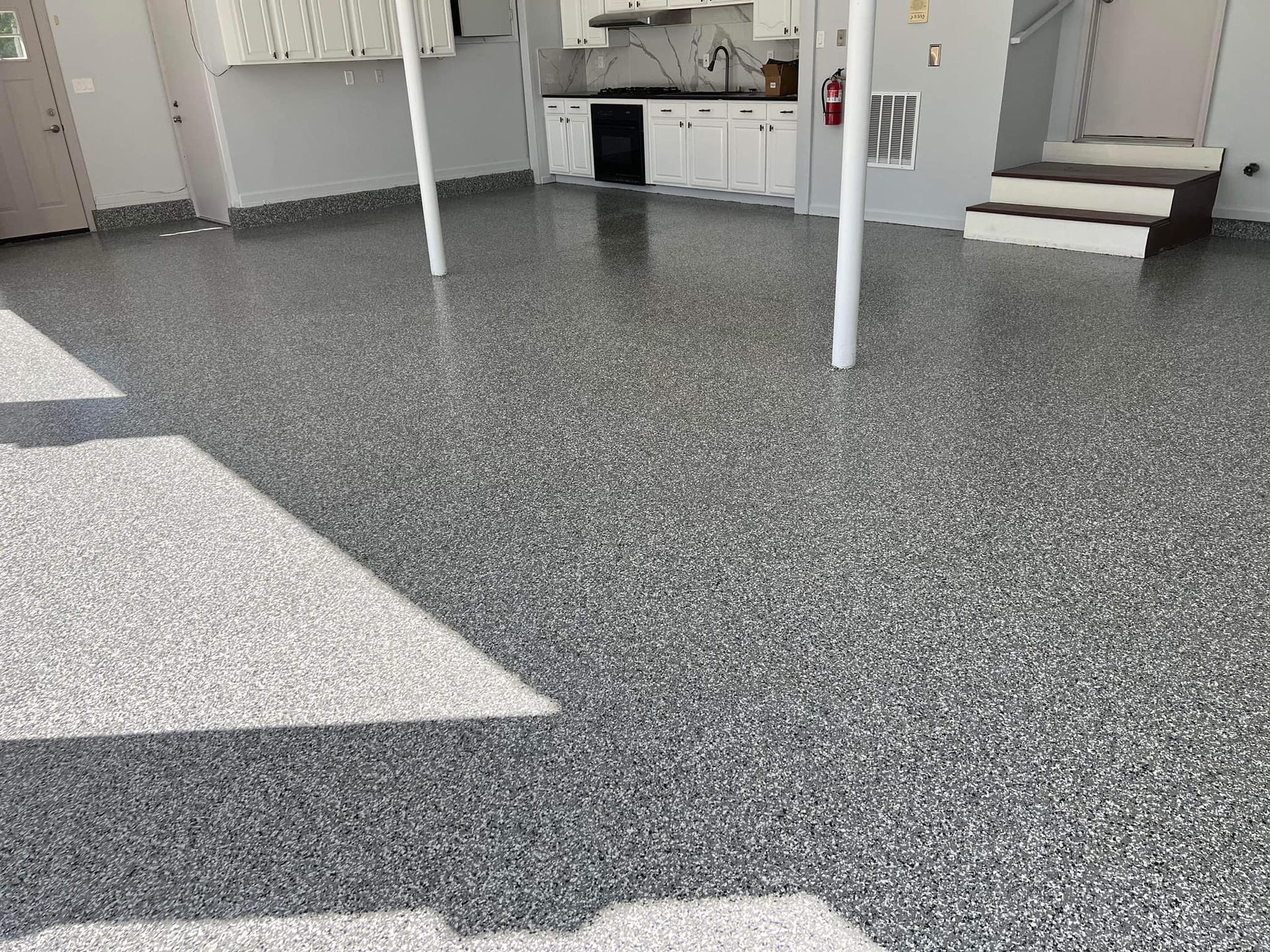Gray speckled epoxy garage floor with white pillars and cabinets.