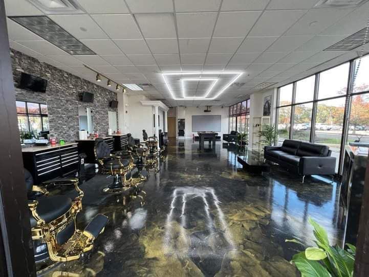 Interior view of a barbershop with black and gold chairs, shiny floor, and large windows.