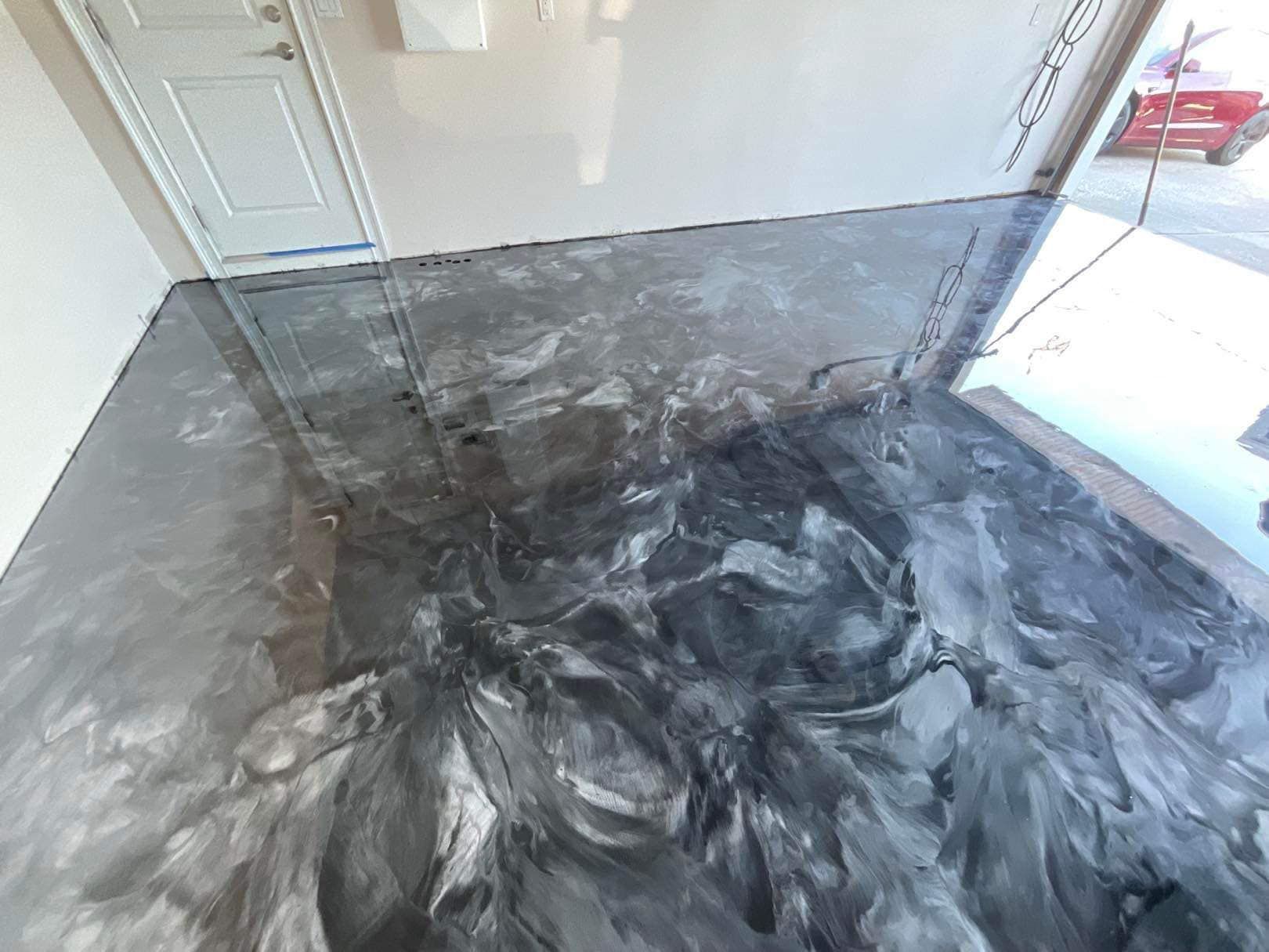 Metallic epoxy garage floor in shades of gray, white door, and bright sunlight.