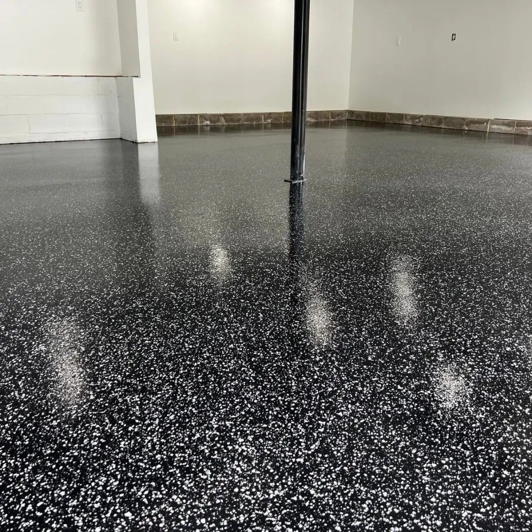 Black epoxy garage floor with silver flakes, reflecting light. Interior shot with a black pole.