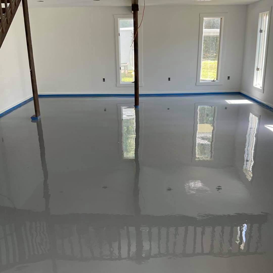 Gray epoxy floor in a room with white walls, windows, and wooden support beams; reflecting the interior.