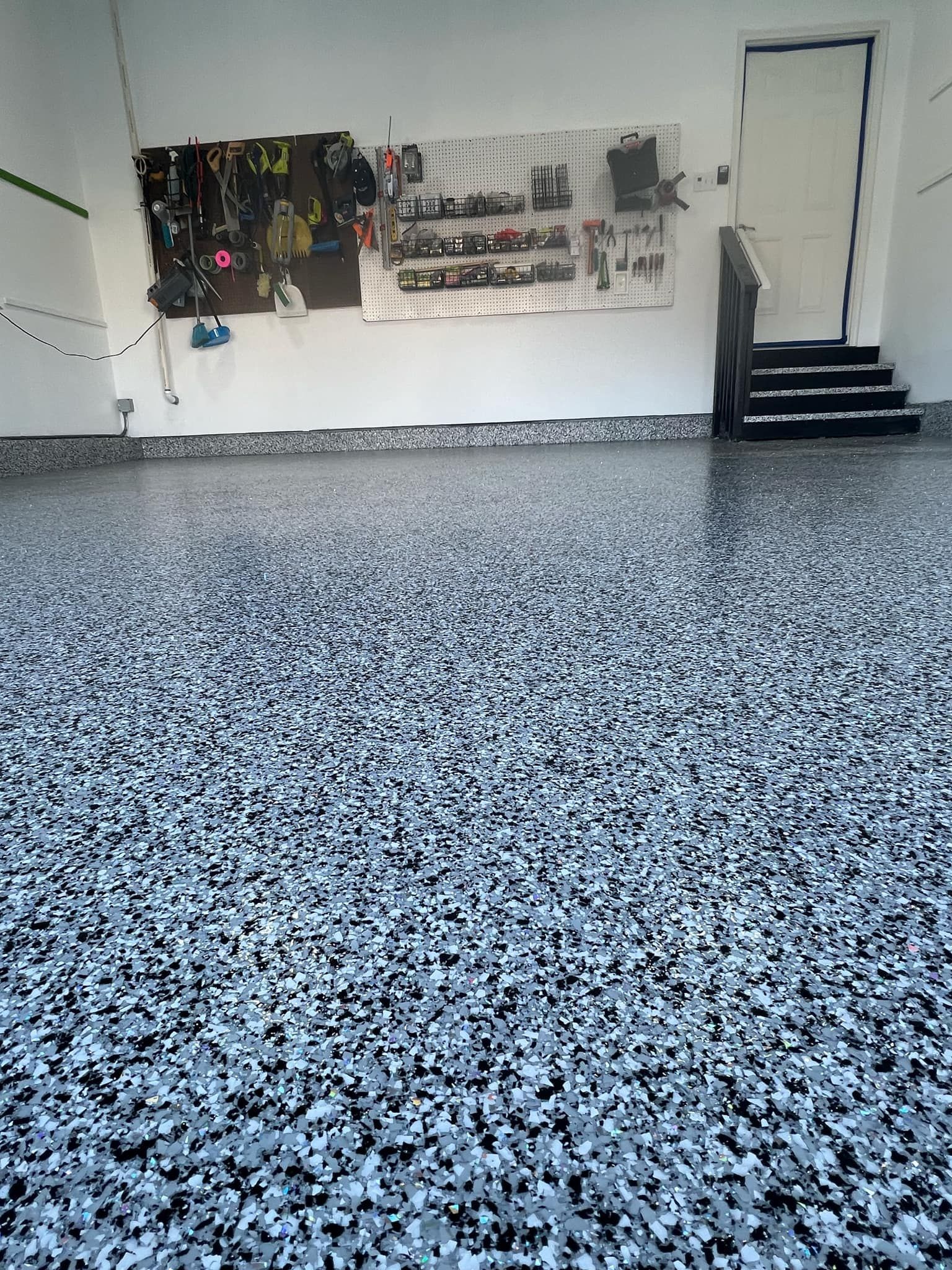 Garage with epoxy speckled floor, pegboard tools, and a door with stairs leading up.