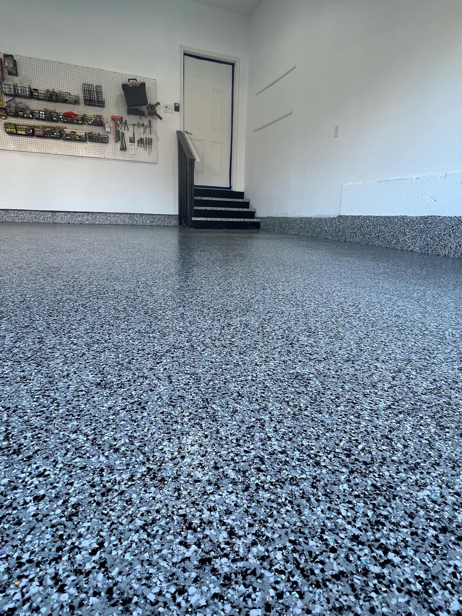Garage with a speckled epoxy floor, tools on wall, and door to an upper level.