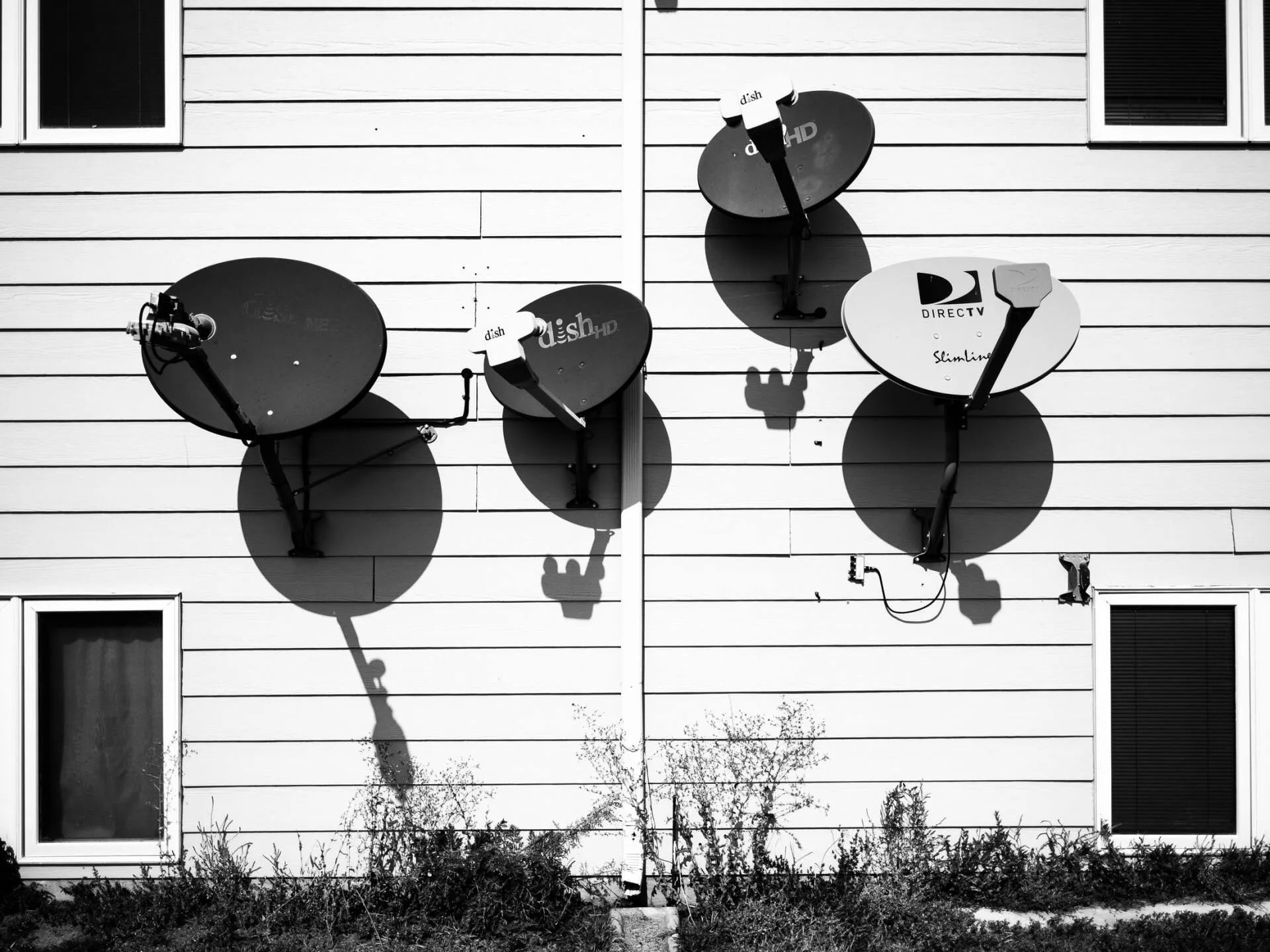Satellite dishes attached to the side of a building, casting long shadows on the exterior.