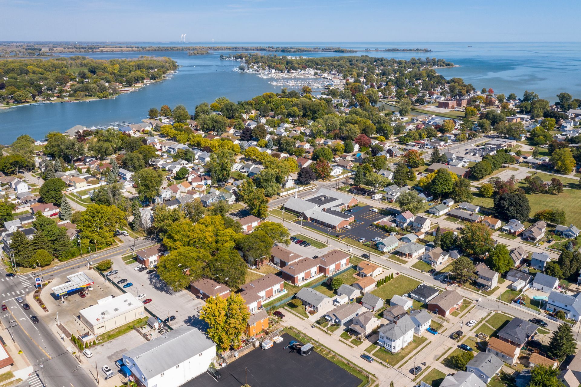 Aerial view of a lakeside town with houses, trees, and a marina under a bright sky.