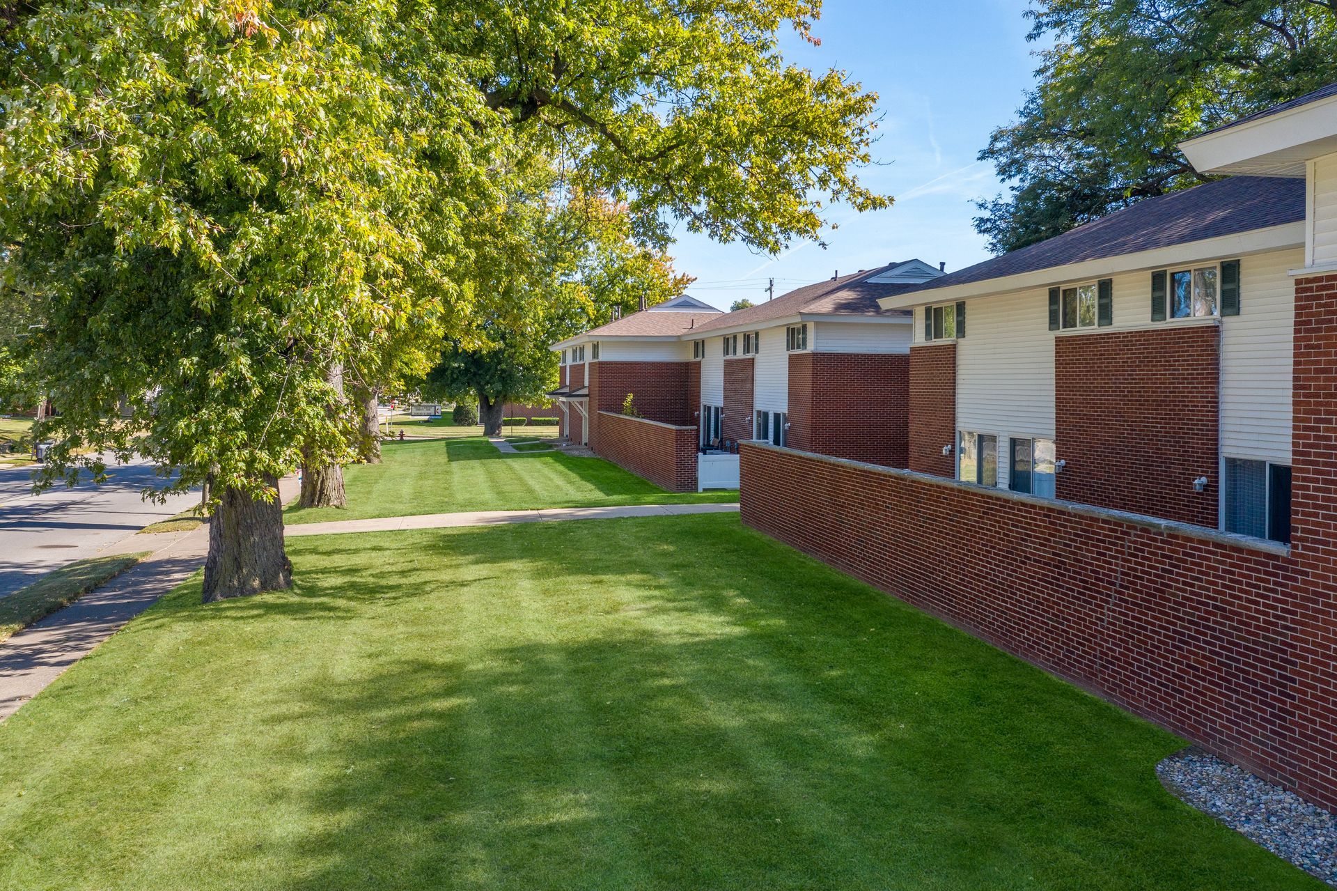 Row of brick townhouses with green lawn and trees.