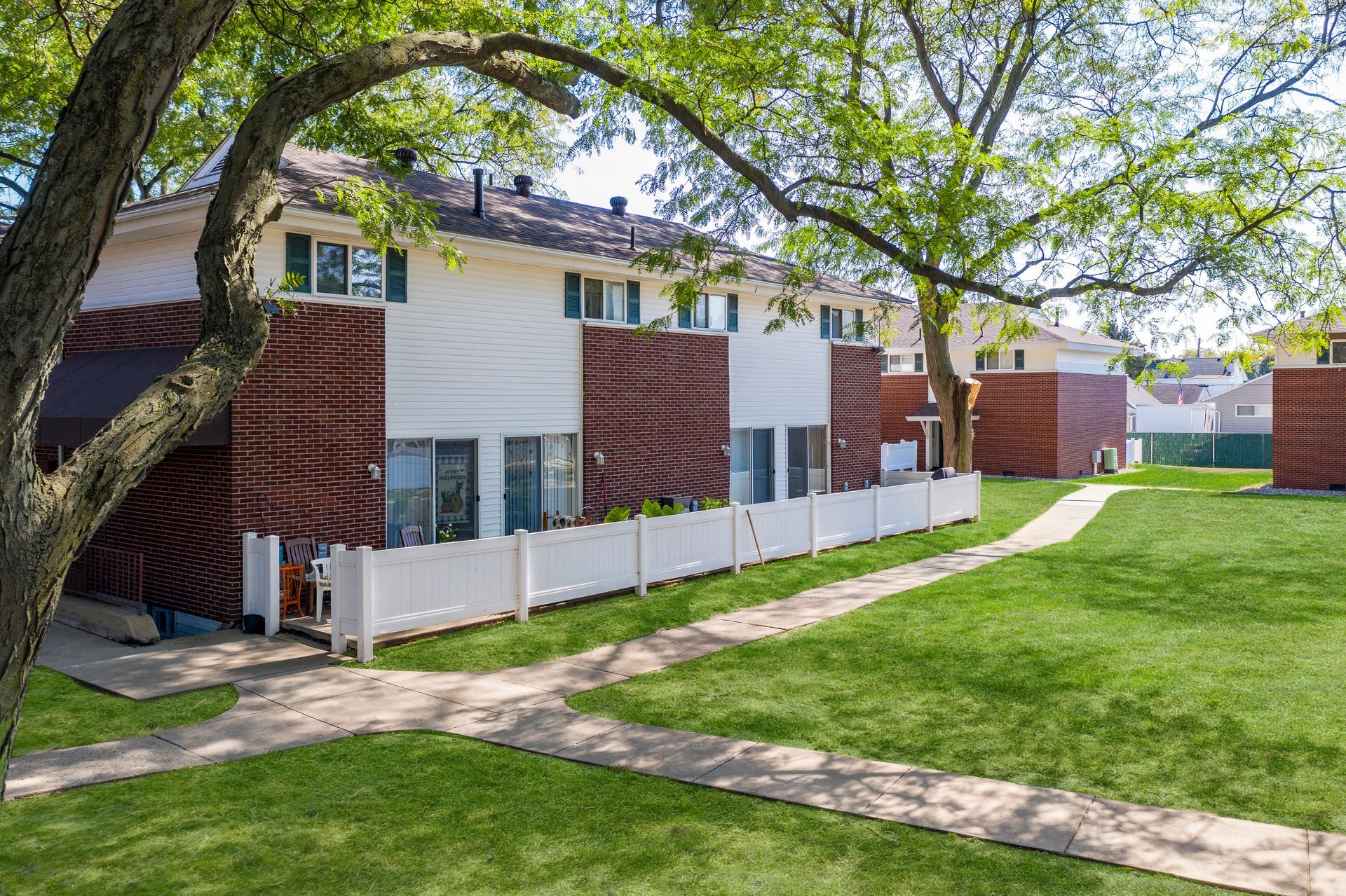 Townhomes with brick and white siding, white picket fence, and green lawn.