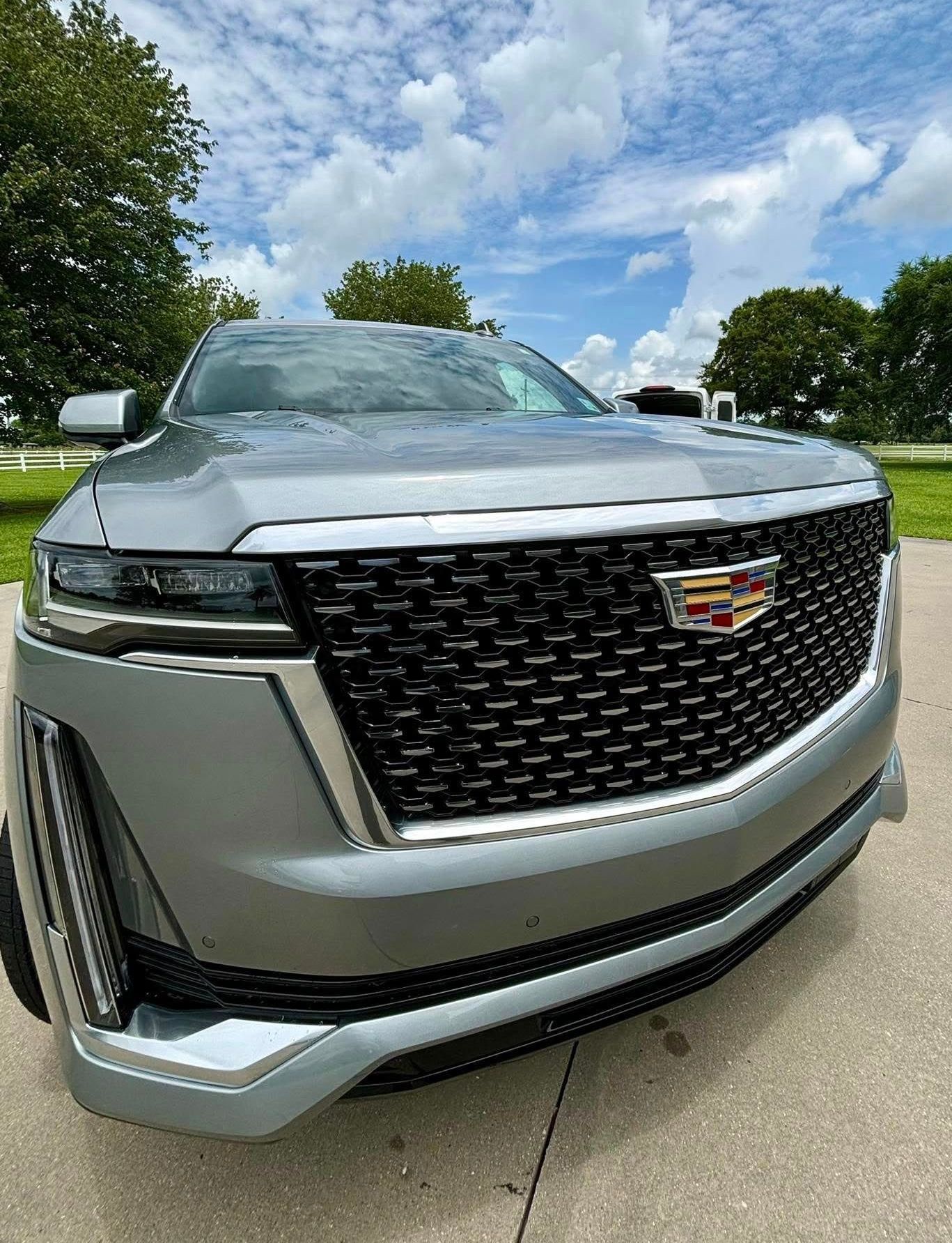 A silver cadillac escalade is parked on the side of the road.