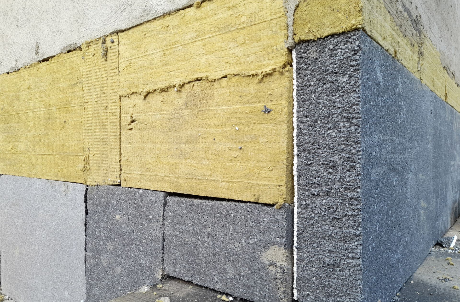 Costruzione del muro esterno con blocchi grigi, isolamento giallo e schiuma grigia.