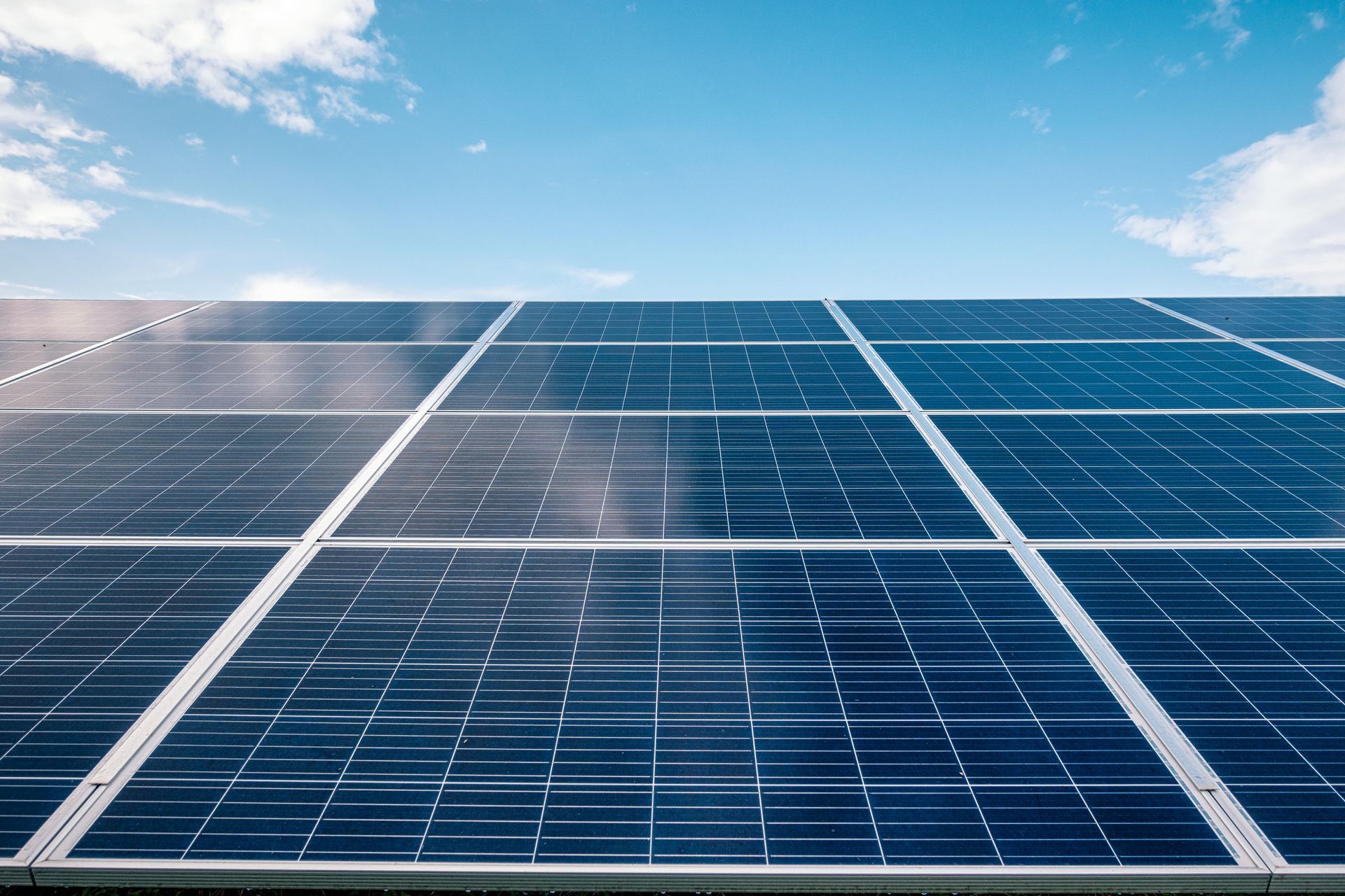 Pannelli solari contro un cielo azzurro con nuvole bianche, che generano energia rinnovabile.