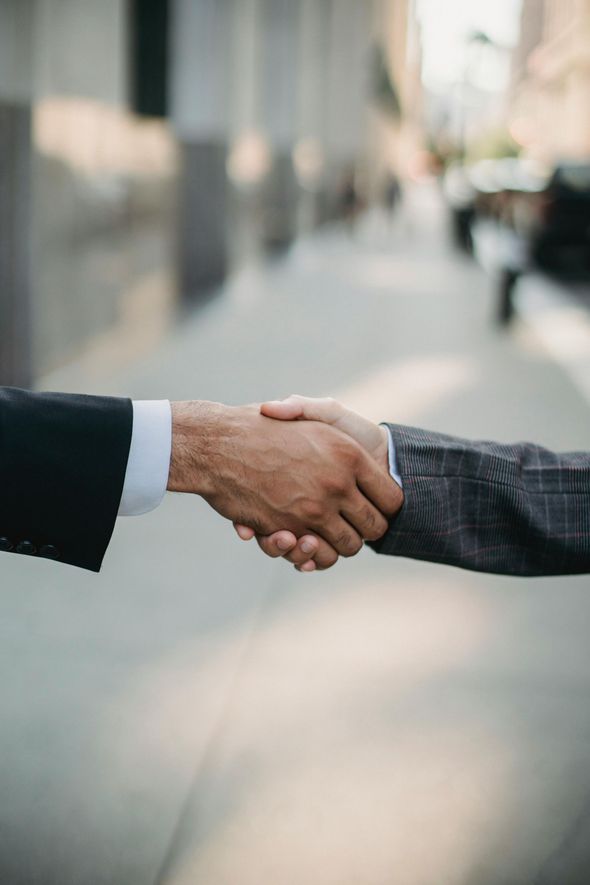 Due persone in giacca e cravatta si stringono la mano su un marciapiede.