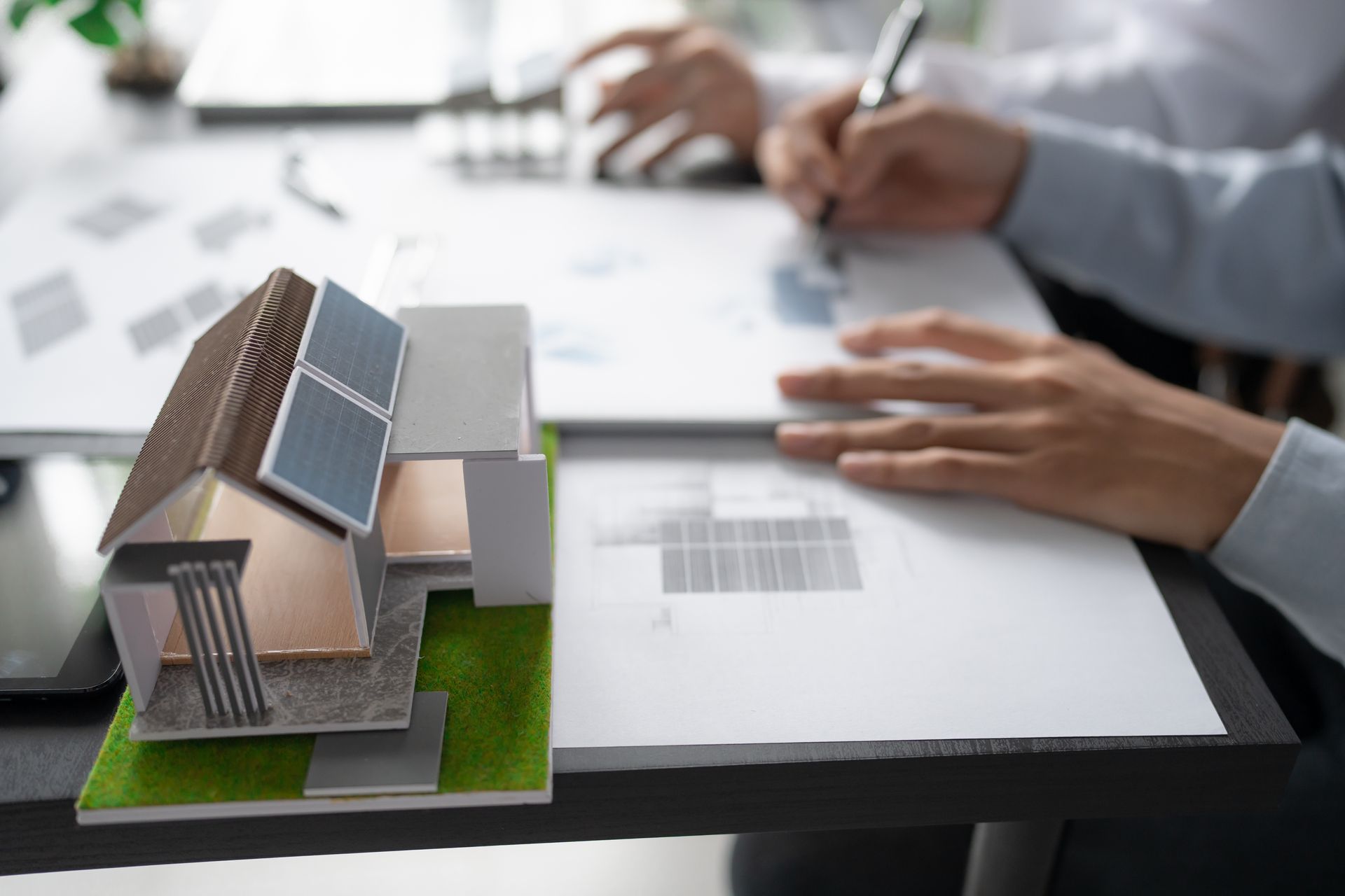 Modello di casa con pannelli solari su una scrivania mentre le persone esaminano i documenti.