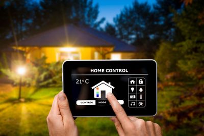 Persona che usa un tablet per controllare una casa intelligente. La casa è illuminata sullo sfondo.