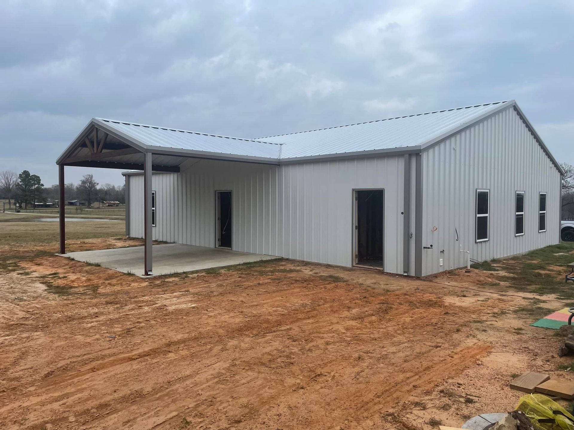 A white metal building with a porch and a carport in a dirt field.