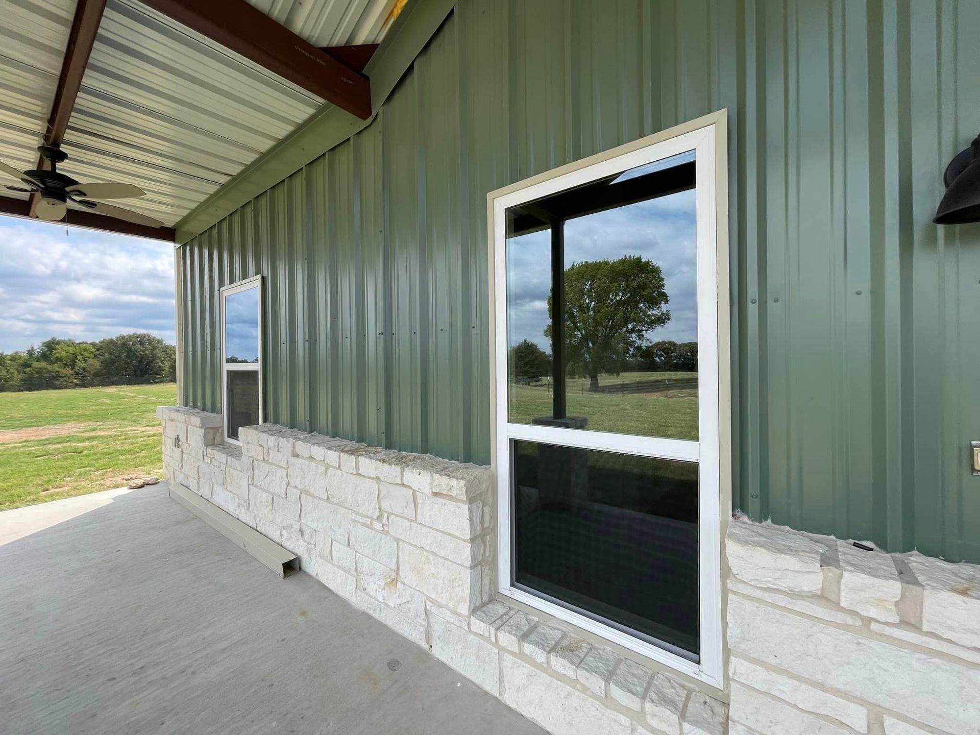 A green metal building with a white window and a brick wall.