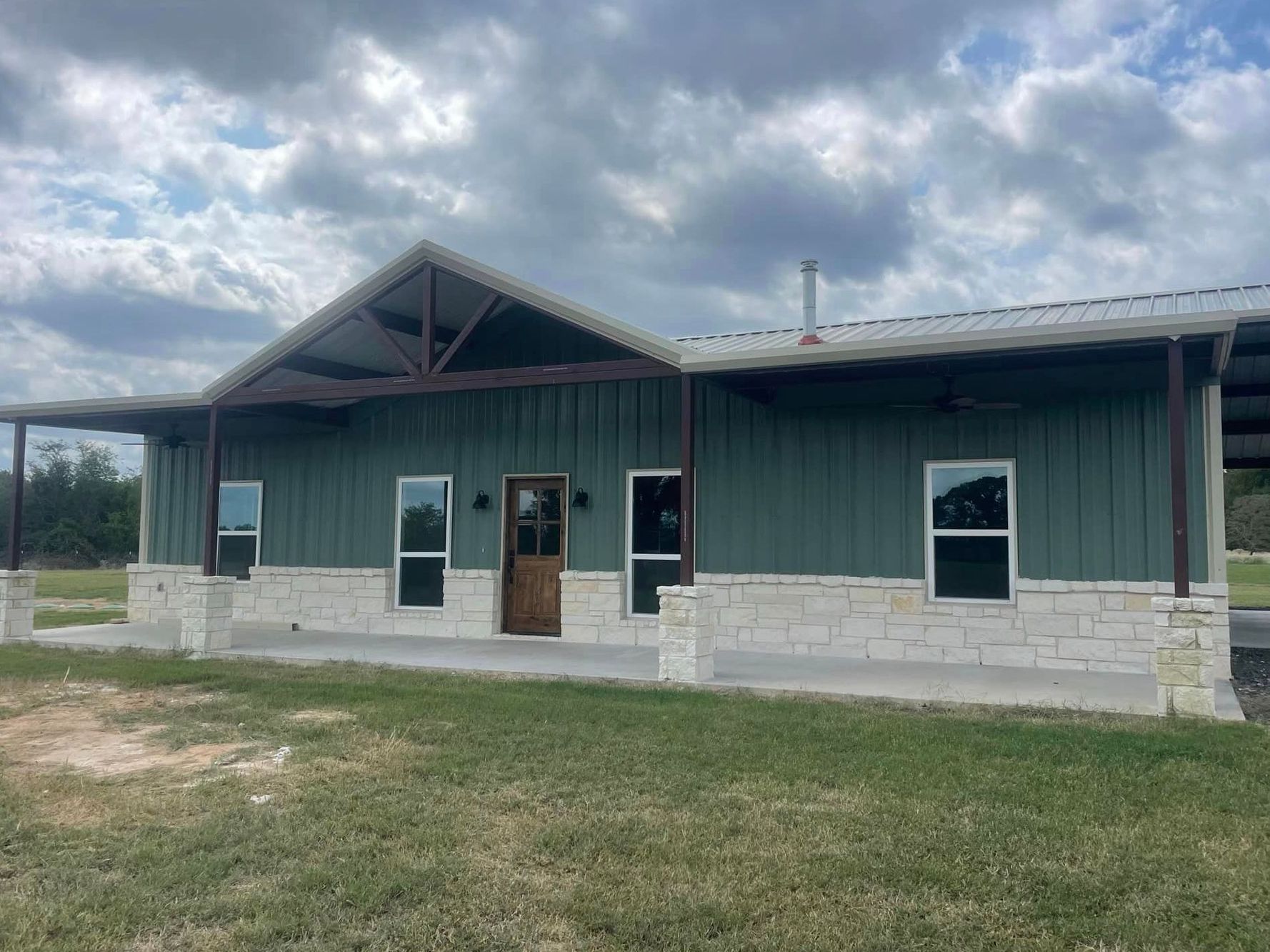 A large green house with a porch and a lot of windows is sitting on top of a lush green field.