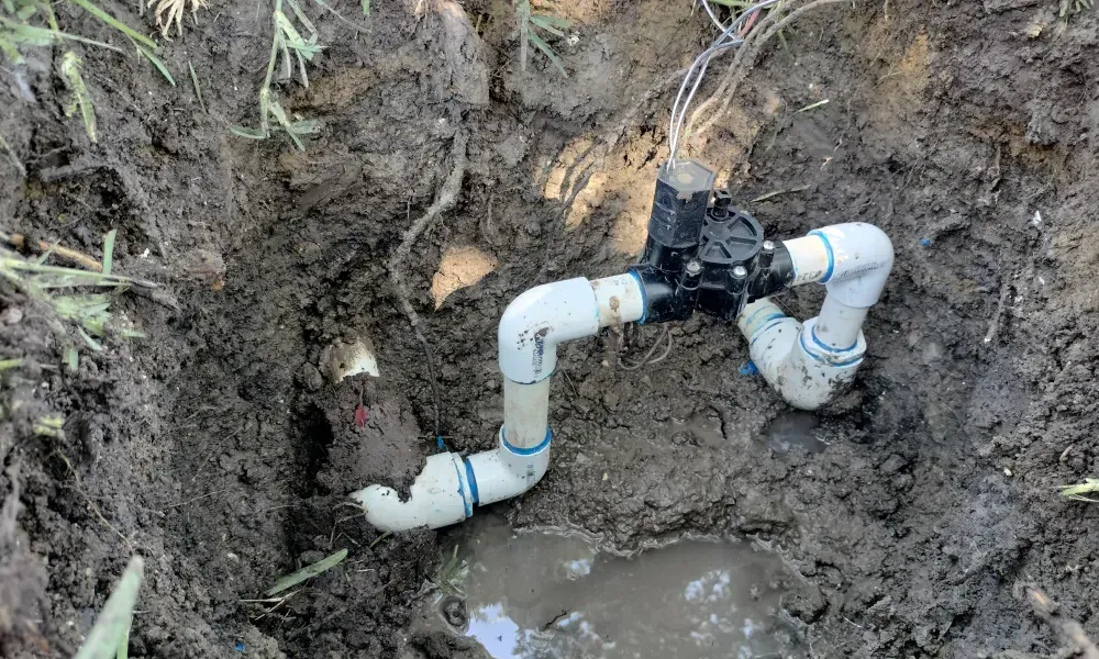 Irrigation valve in muddy ground with white PVC pipes.