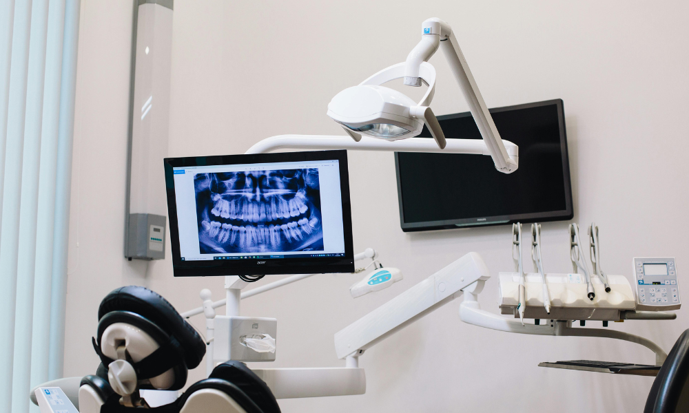 Dentist pointing to tooth on a panoramic X-ray displayed on a computer screen.