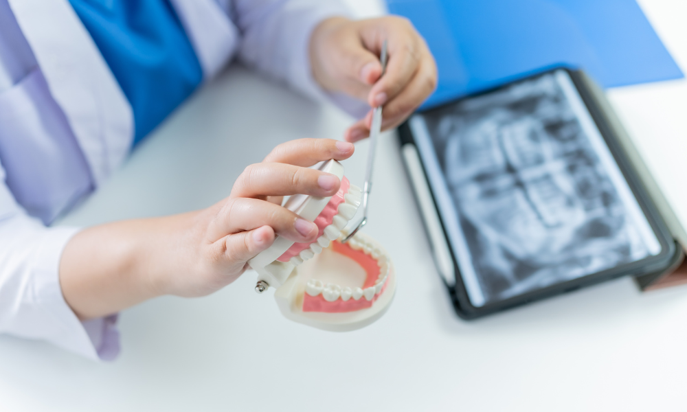 Dentist pointing to tooth on a panoramic X-ray displayed on a computer screen.