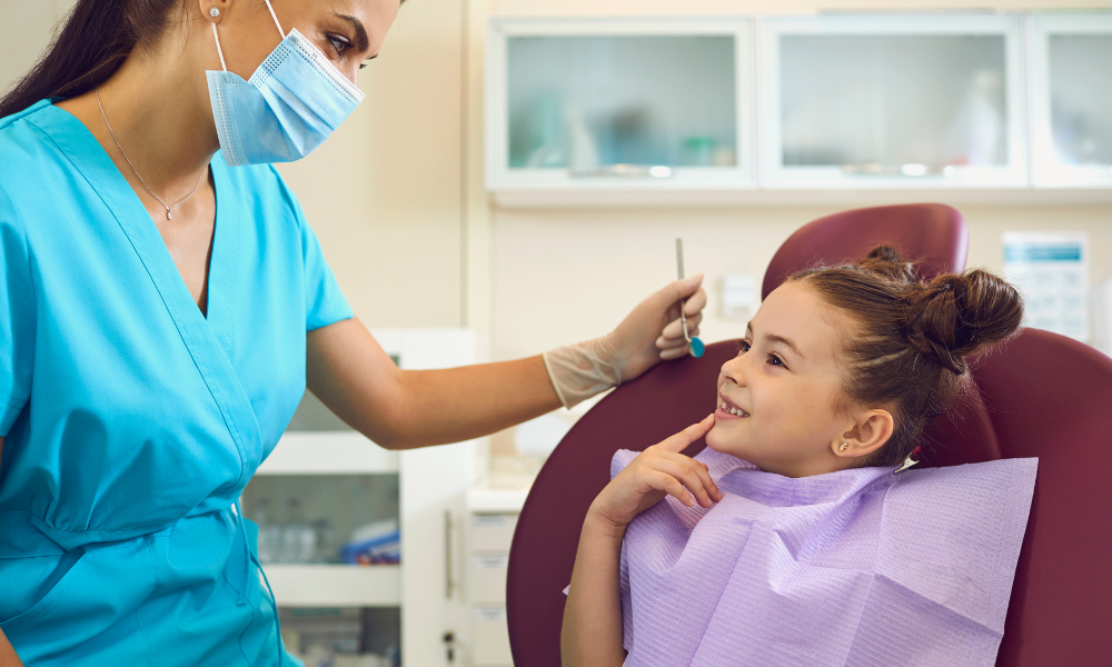 Dentist pointing to tooth on a panoramic X-ray displayed on a computer screen.