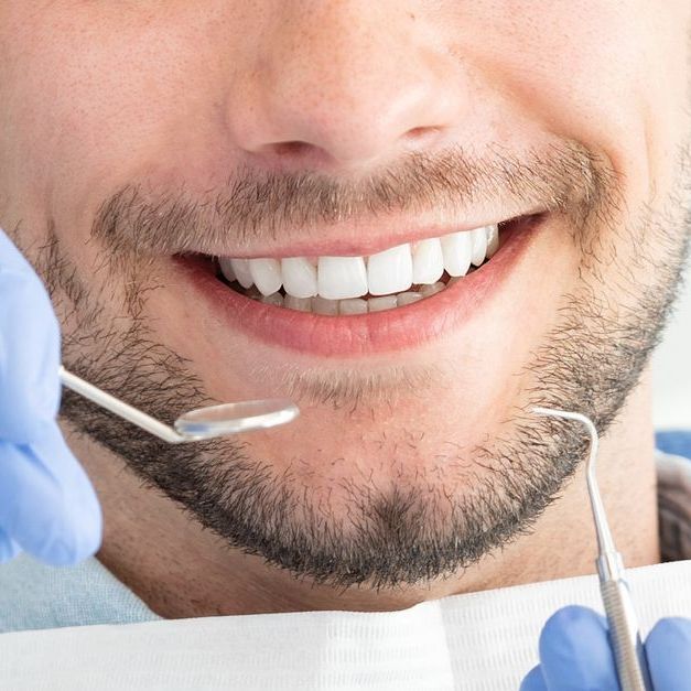 Man at a dental appointment with a bright smile, tools in hands.