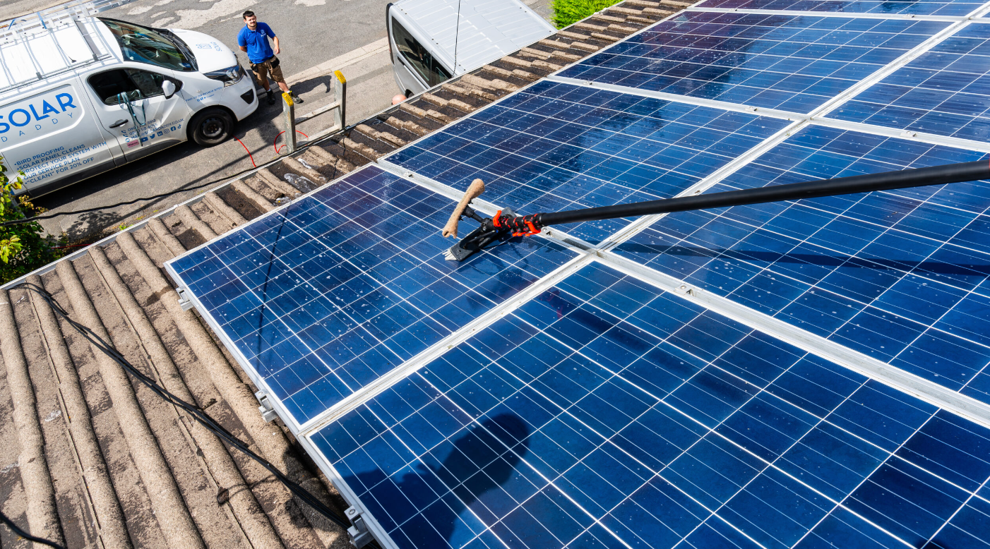 A man is cleaning solar panels on the roof of a house.