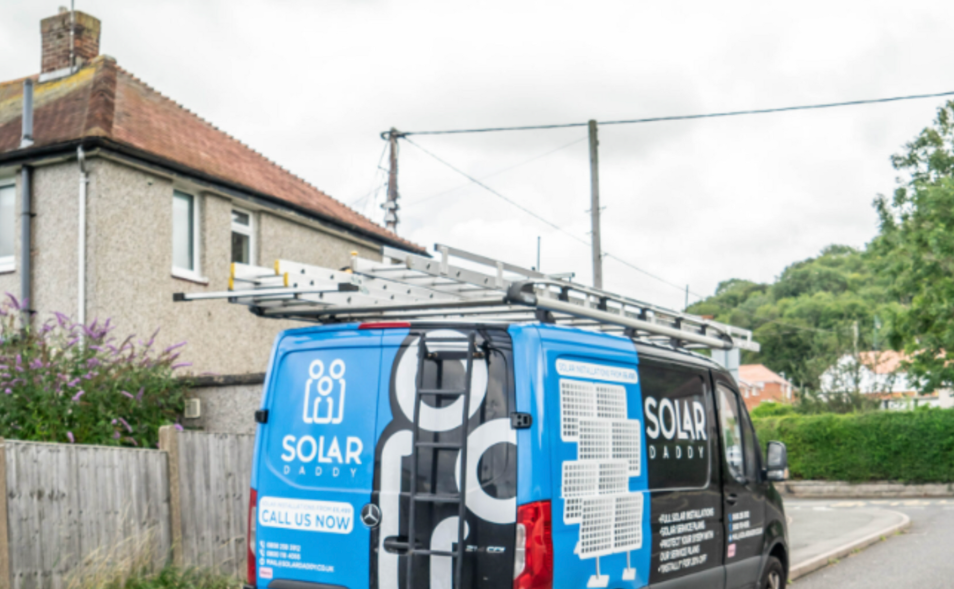 A blue van with a ladder on top of it is parked in front of a house.