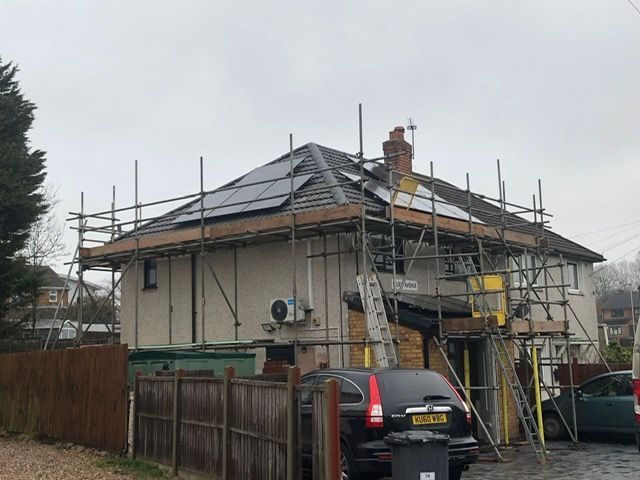 A car is parked in front of a house with scaffolding on the roof.